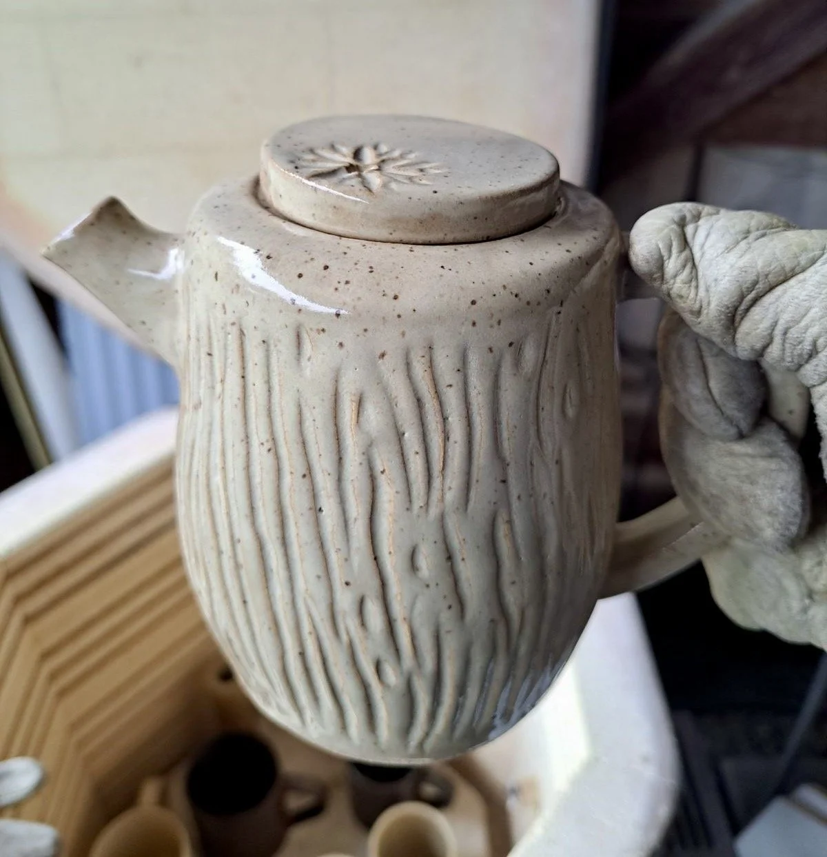 A ceramic teapot with a textured, bark-like surface design, held by a gloved hand.