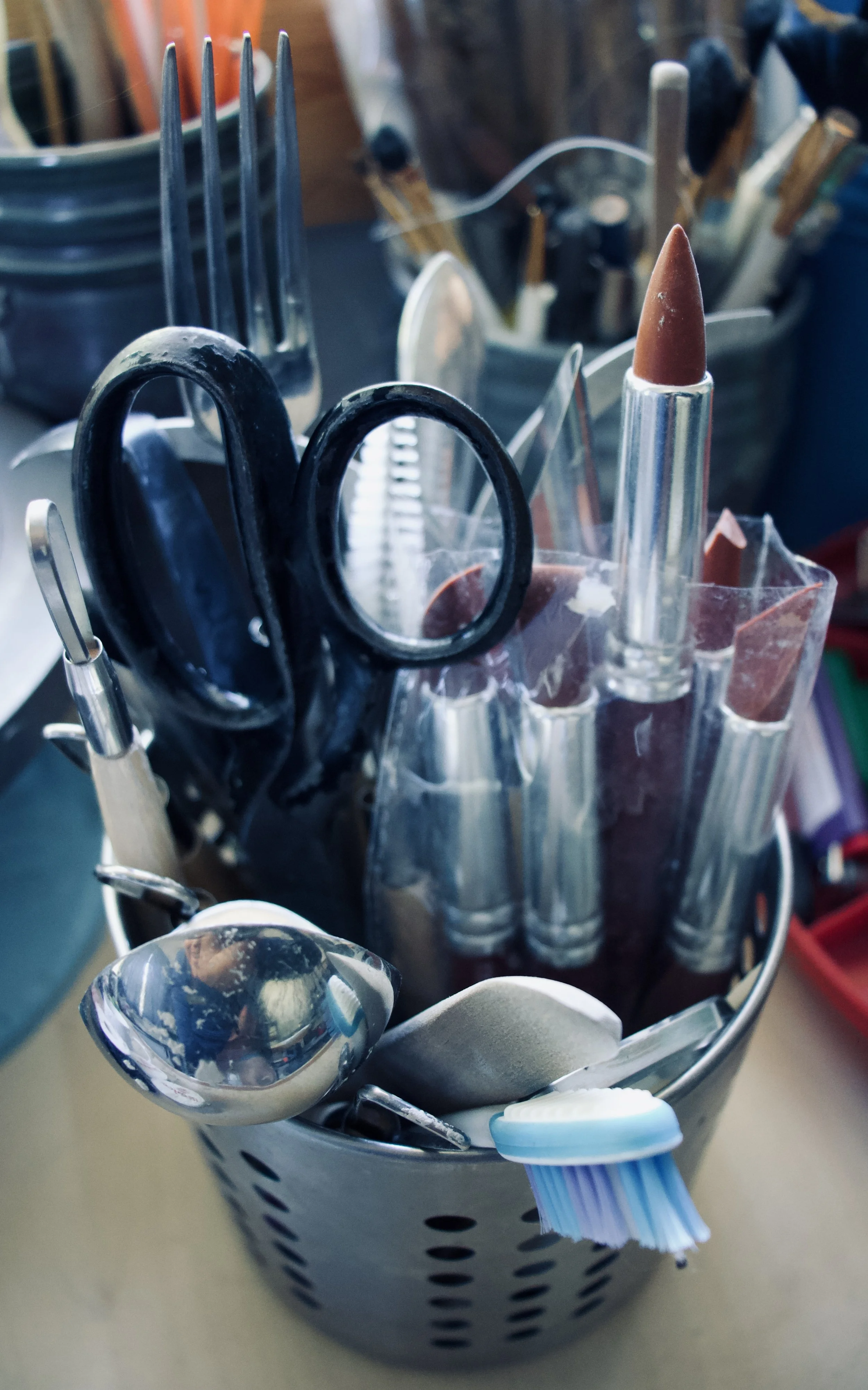 A metal container holding various dental tools, including scissors, a toothbrush, a pair of tweezers, and several large brushes, on a beige surface.