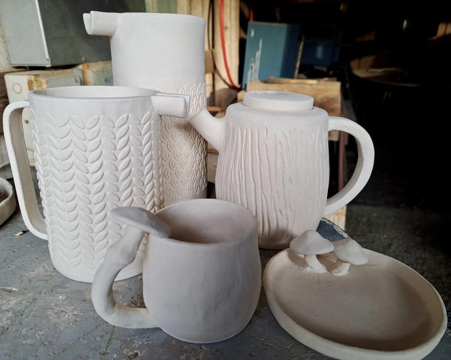 Unfinished white ceramic mugs and a small dish on a work table in a pottery studio.