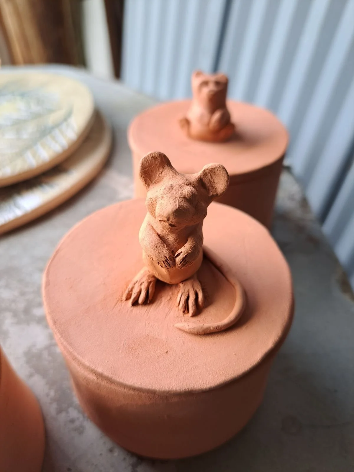 Terracotta pots with mouse sculptures on top, set on a weathered wooden table.