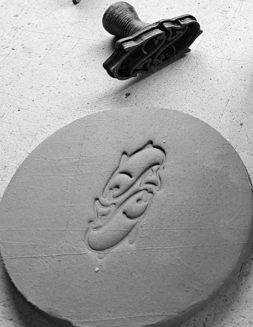 A round soap with a cartoonish face carved into it, with a black toy vehicle near it on a textured surface.