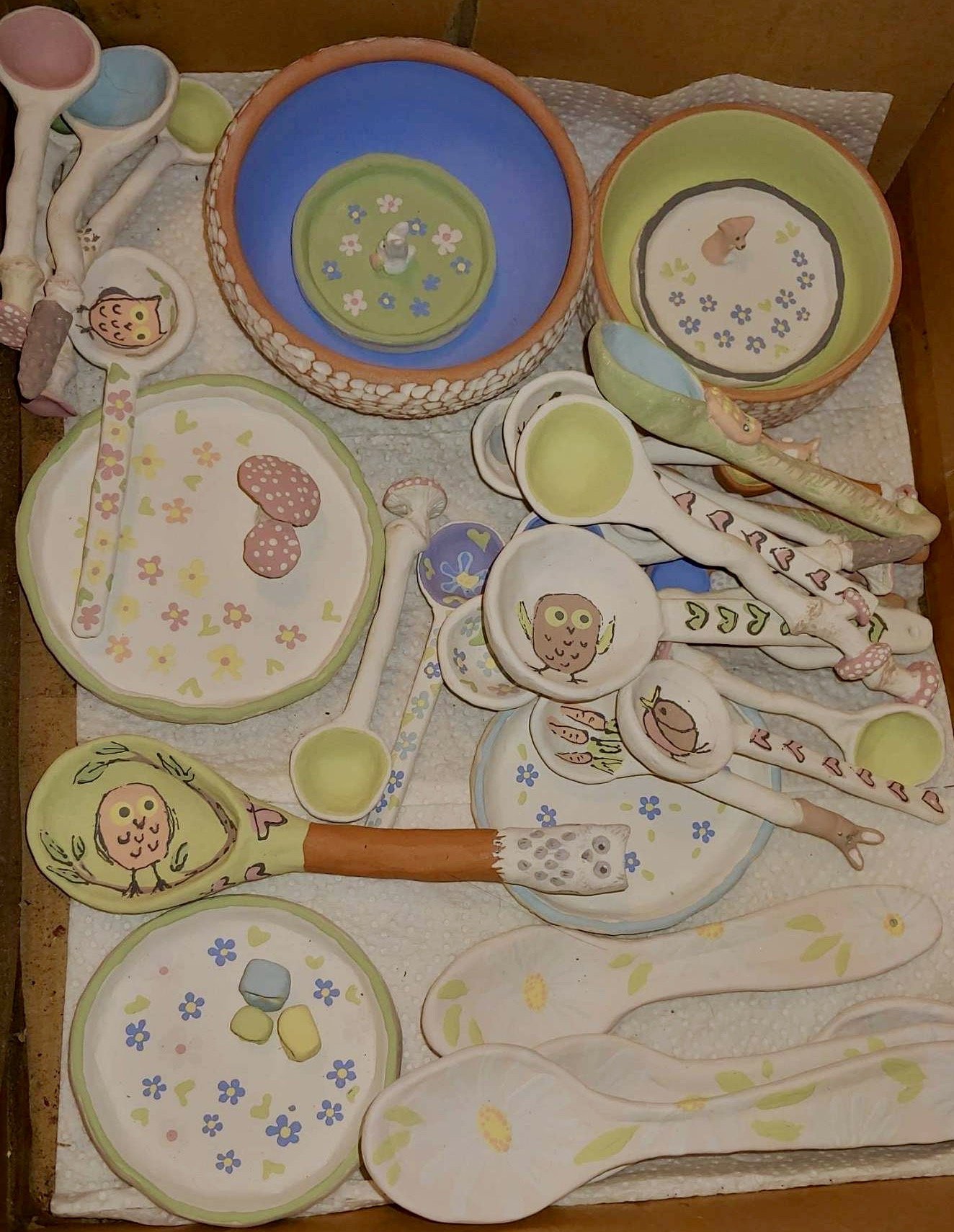 Colorful painted ceramic kitchenware, including bowls, plates, spoons, and ladles with owl and animal designs.