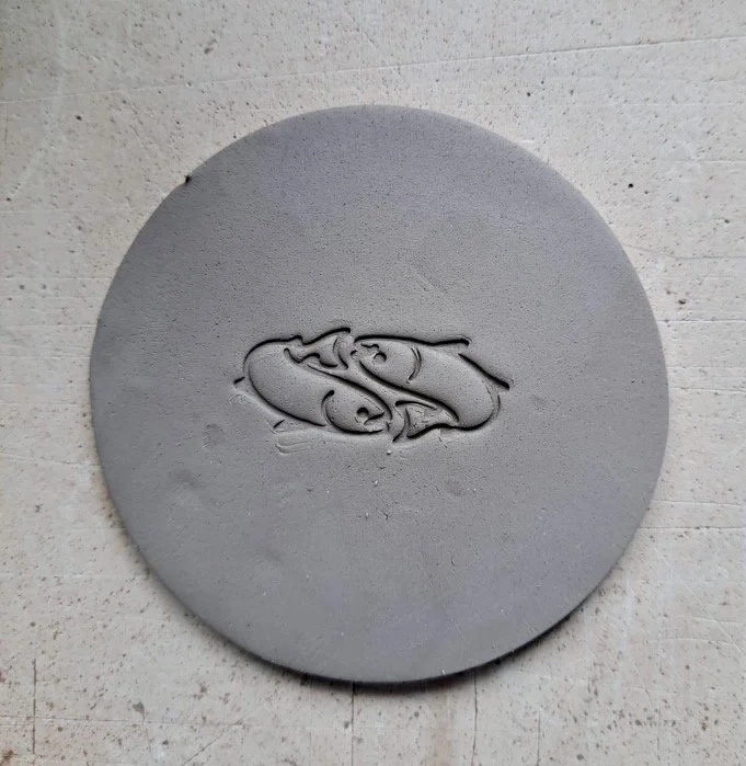 A round gray stone with a carved image of two koi fish swimming in a circular pattern.