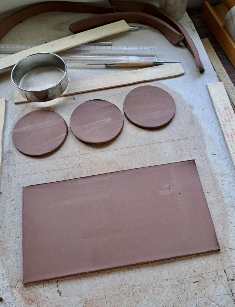 Clay modeling tools and three finished clay coasters on a work surface.