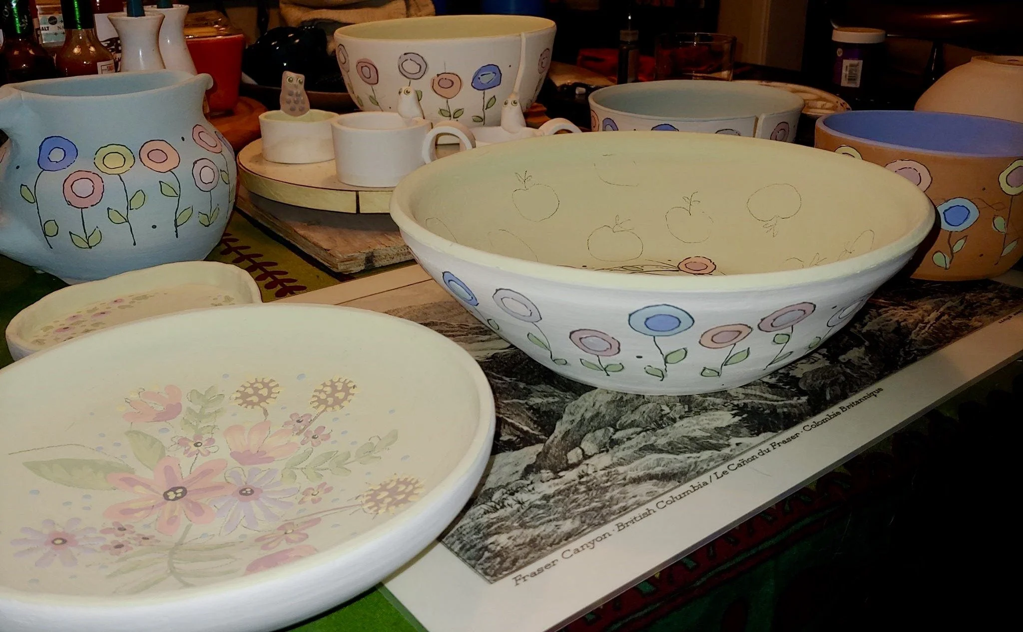 Collection of hand-painted ceramic bowls, vases, and figurines with colorful flower and nature motifs on a table.