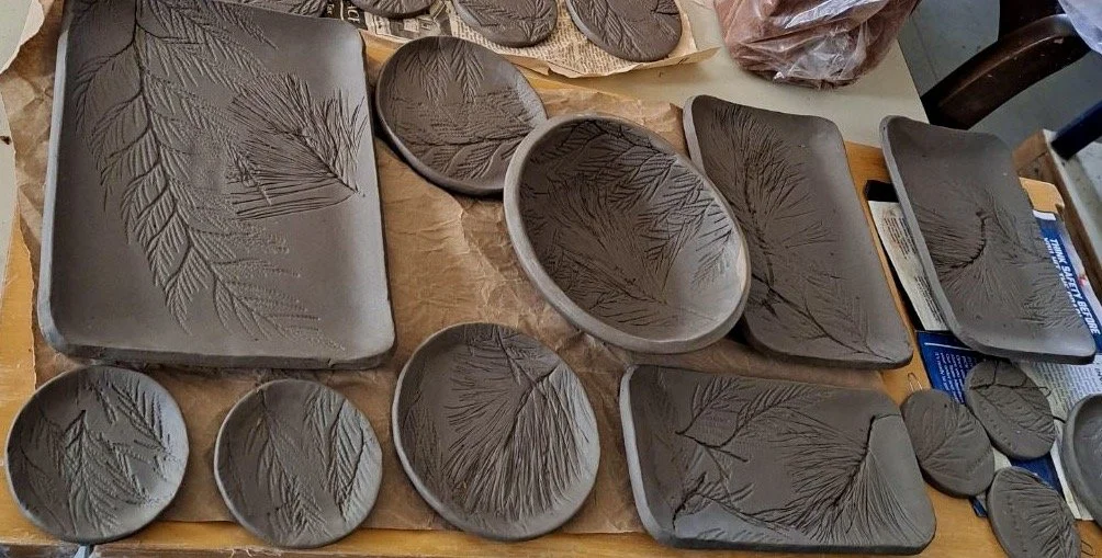Various ceramic bowls and trays with leaf patterns, arranged on a table.