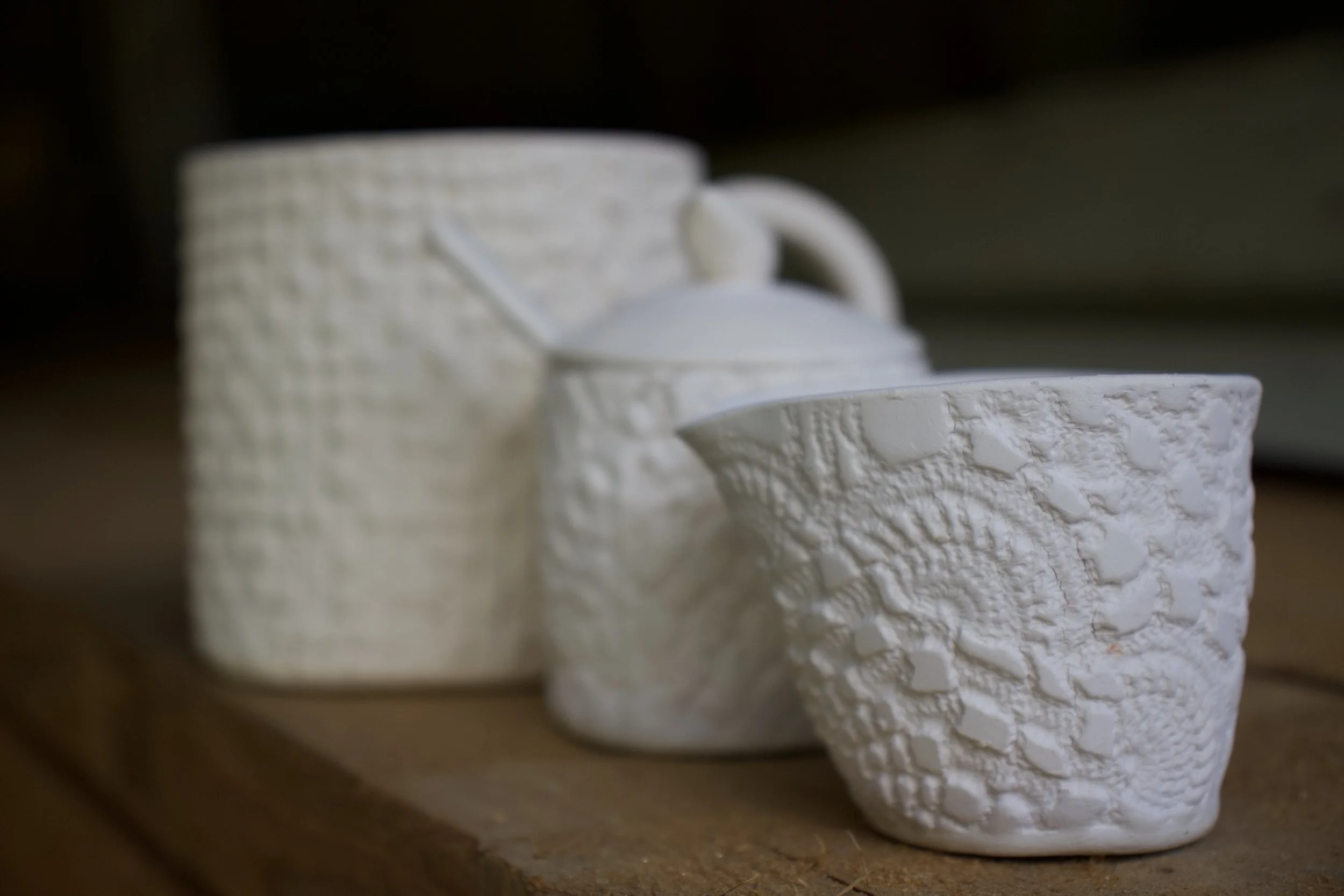 Set of white ceramic mugs with textured patterns on a wooden surface.