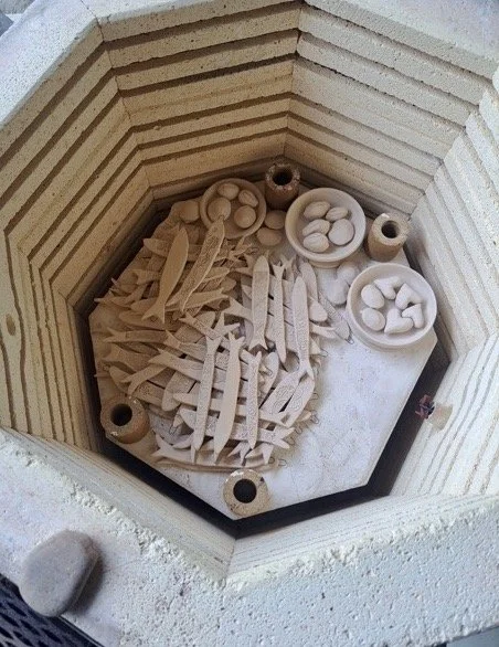 Miniature wooden utensils and small bowls inside a wooden oven or kiln.