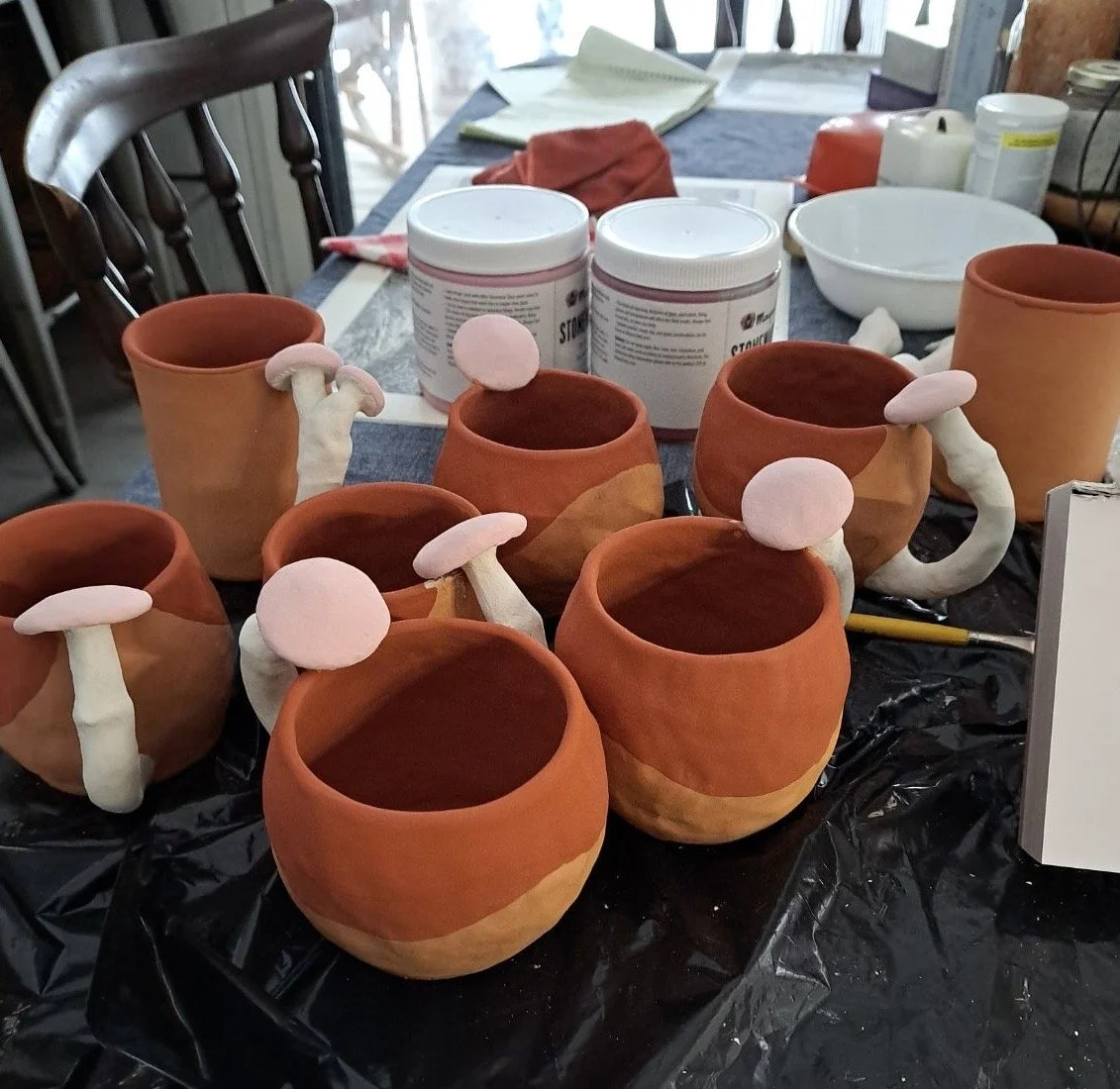 Clay pots shaped like mushrooms with white stems and pink caps on a black table.