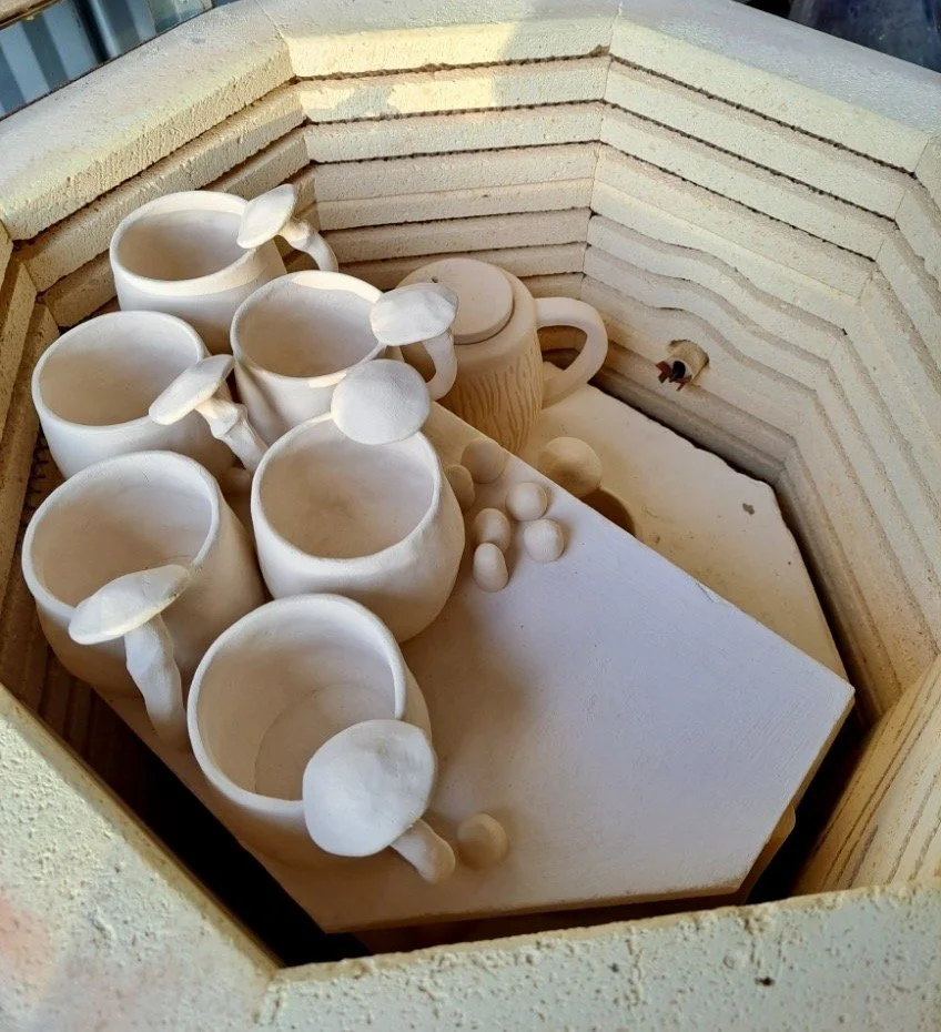 Unfinished ceramic coffee mugs and some small balls of clay in a kiln or mold.