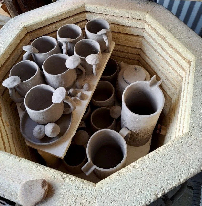 Unfinished pottery mugs and bowls in a kiln.