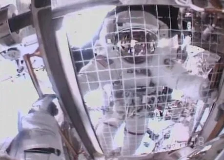 NASA astronaut Barry "Butch" Wilmore in a spacesuit reaching out through the window of a spacecraft or space station, trying to contact or interact with someone outside.