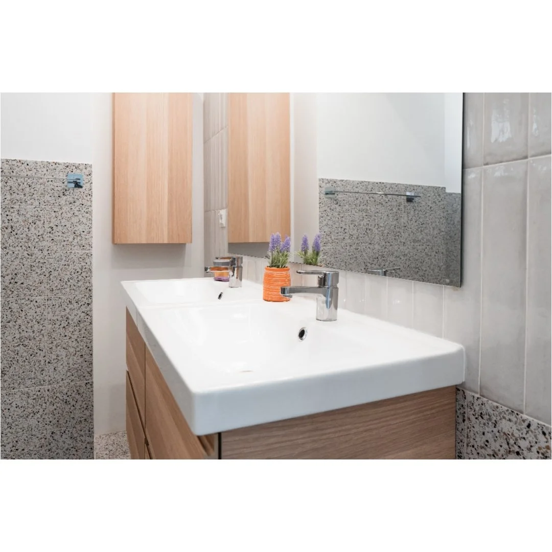 A modern bathroom sink with a large mirror, wooden cabinets, a small plant in orange pot, and lavender flowers.