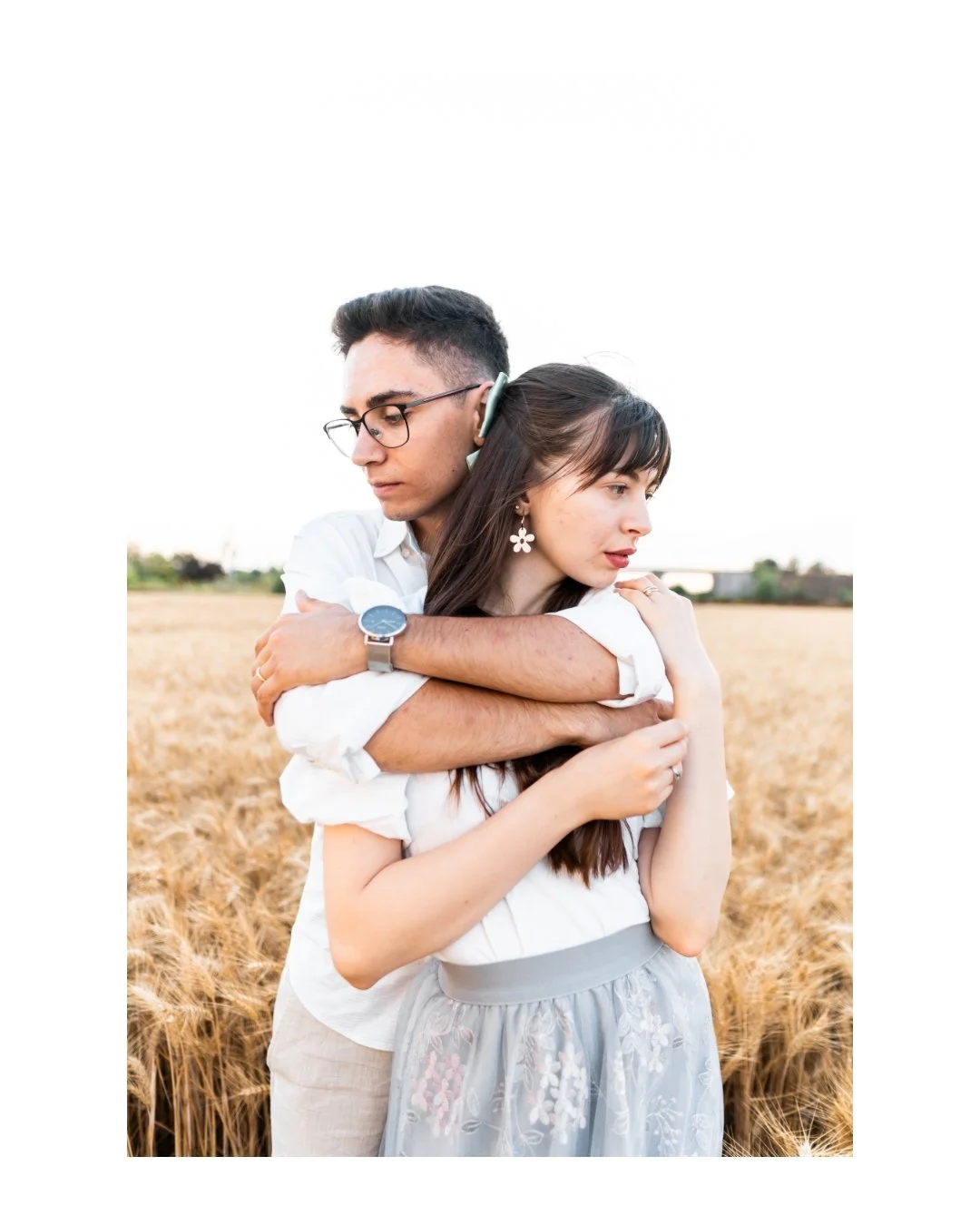 A man hugging a woman from behind in a wheat field during sunset.