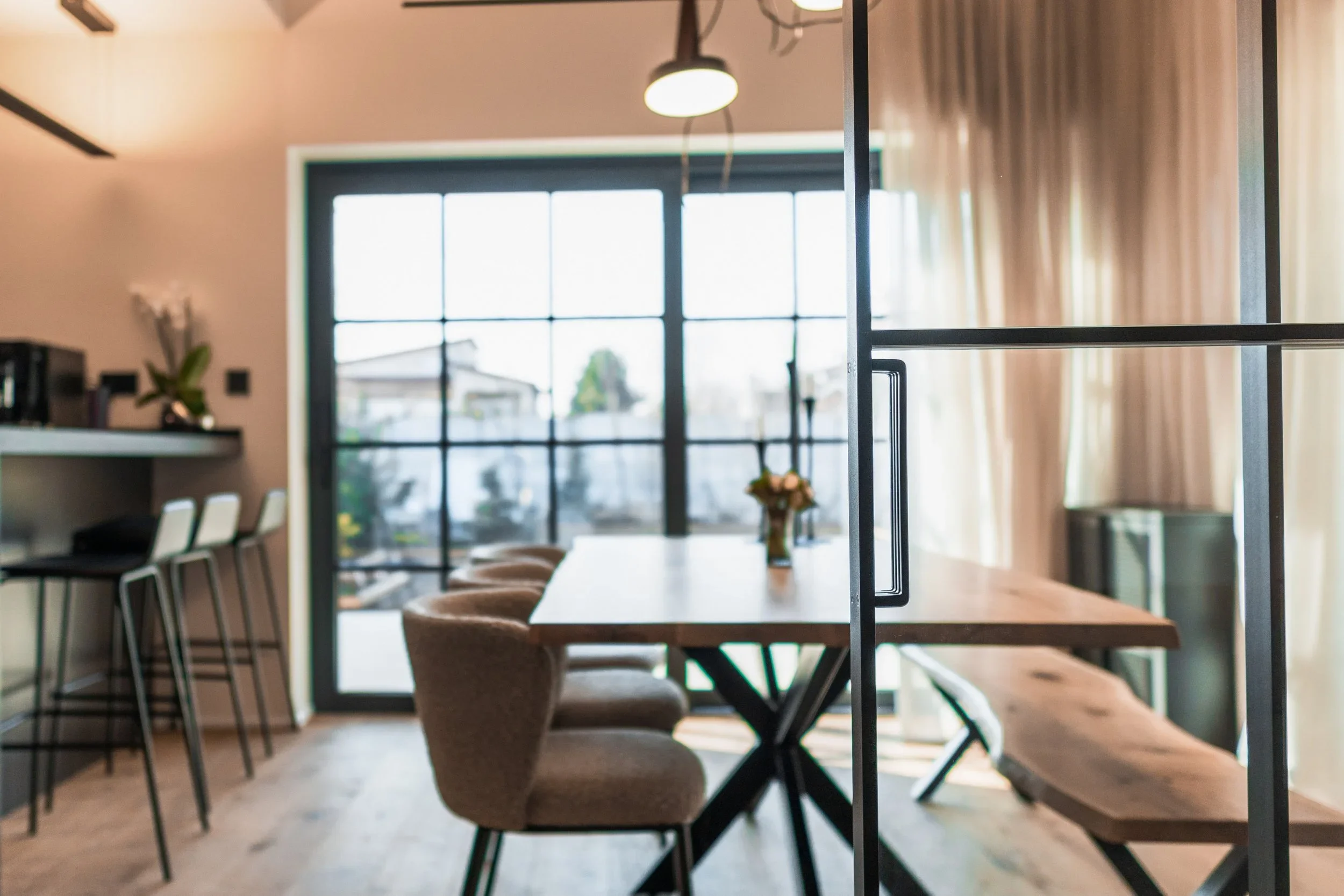 Modern dining area with wooden table, beige chairs, large window, and beige curtains.