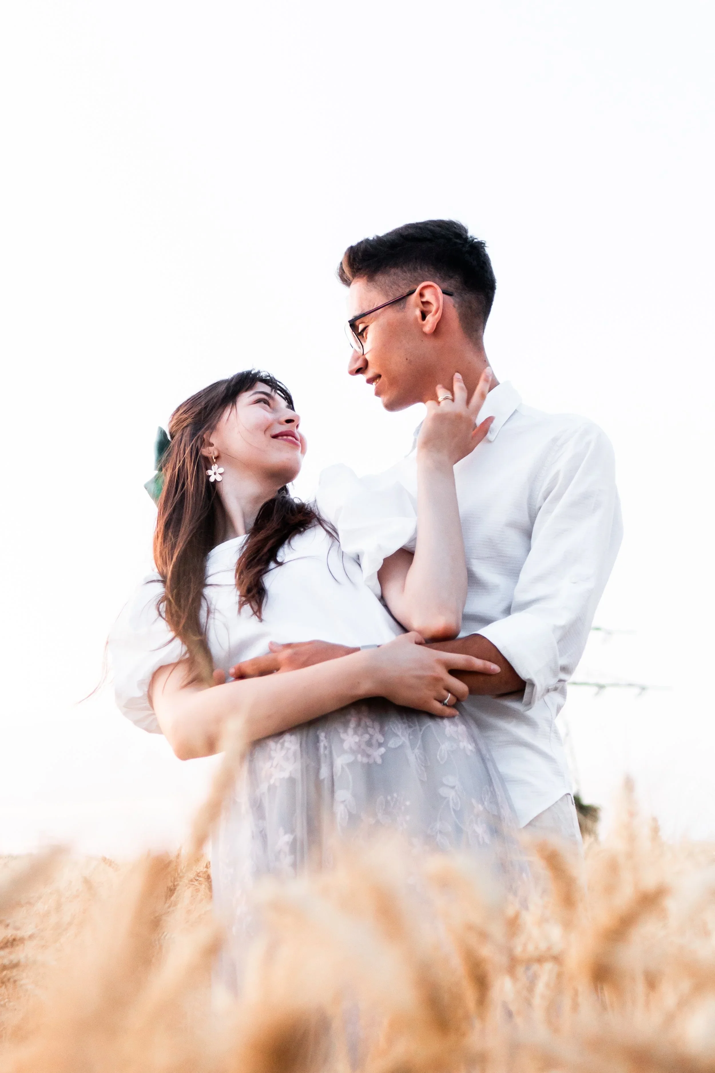 A young couple holding each other and looking into each other's eyes in a wheat field during the daytime.