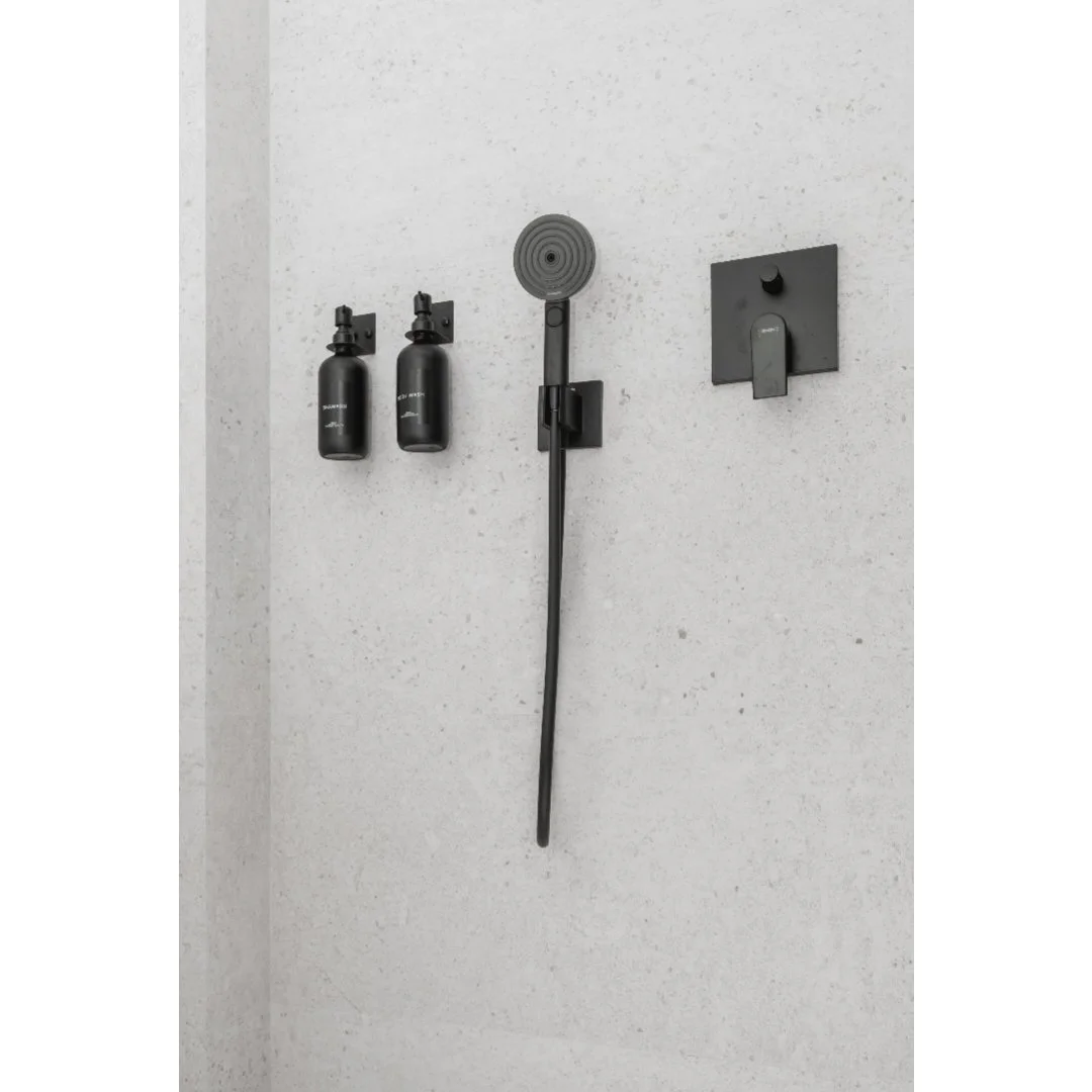 Black showerhead and two black soap or shampoo bottles on a white textured bathroom wall.