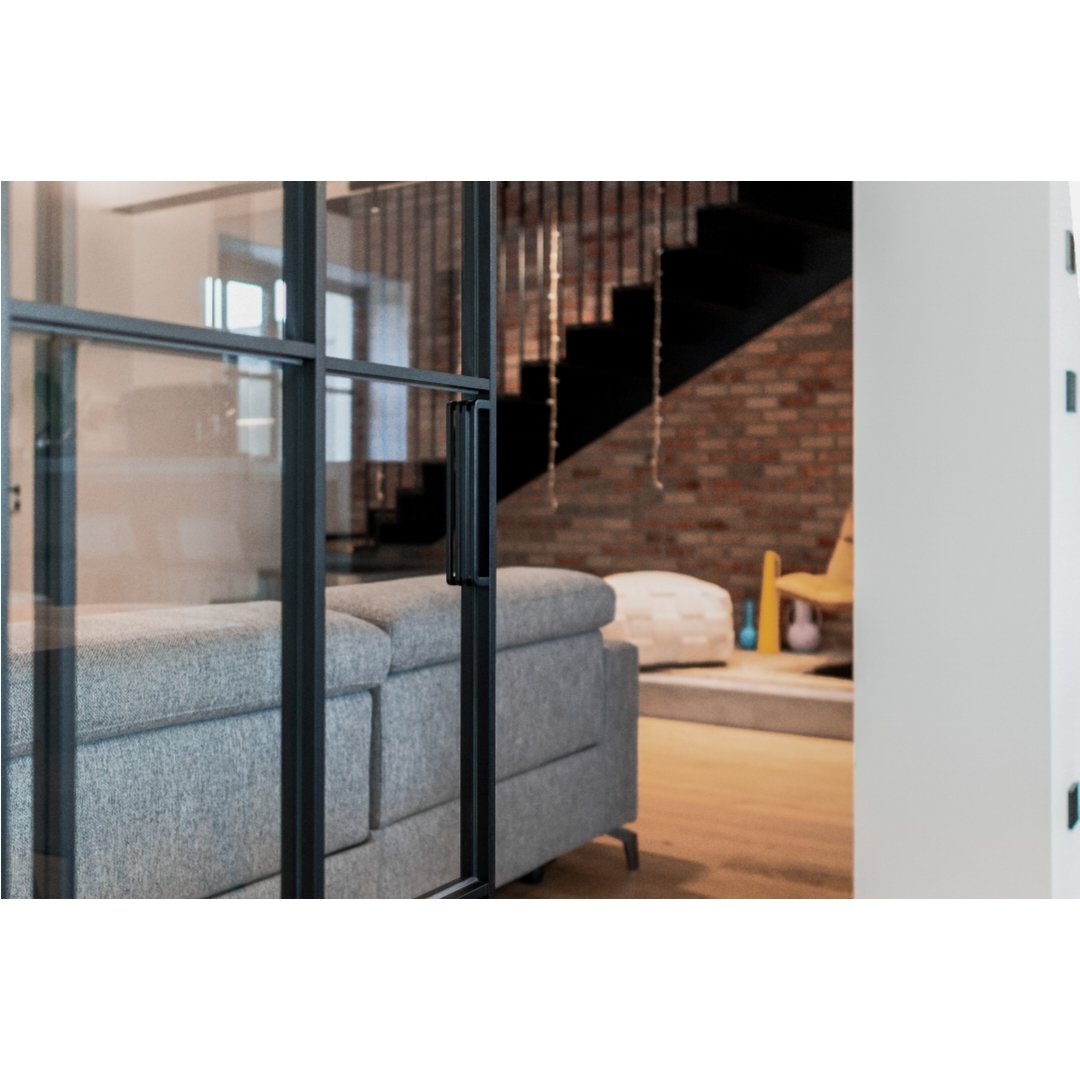 View of a modern living room with a gray sofa, glass partition, wooden stairs with a brick wall background, and a yellow chair with decorative vases.