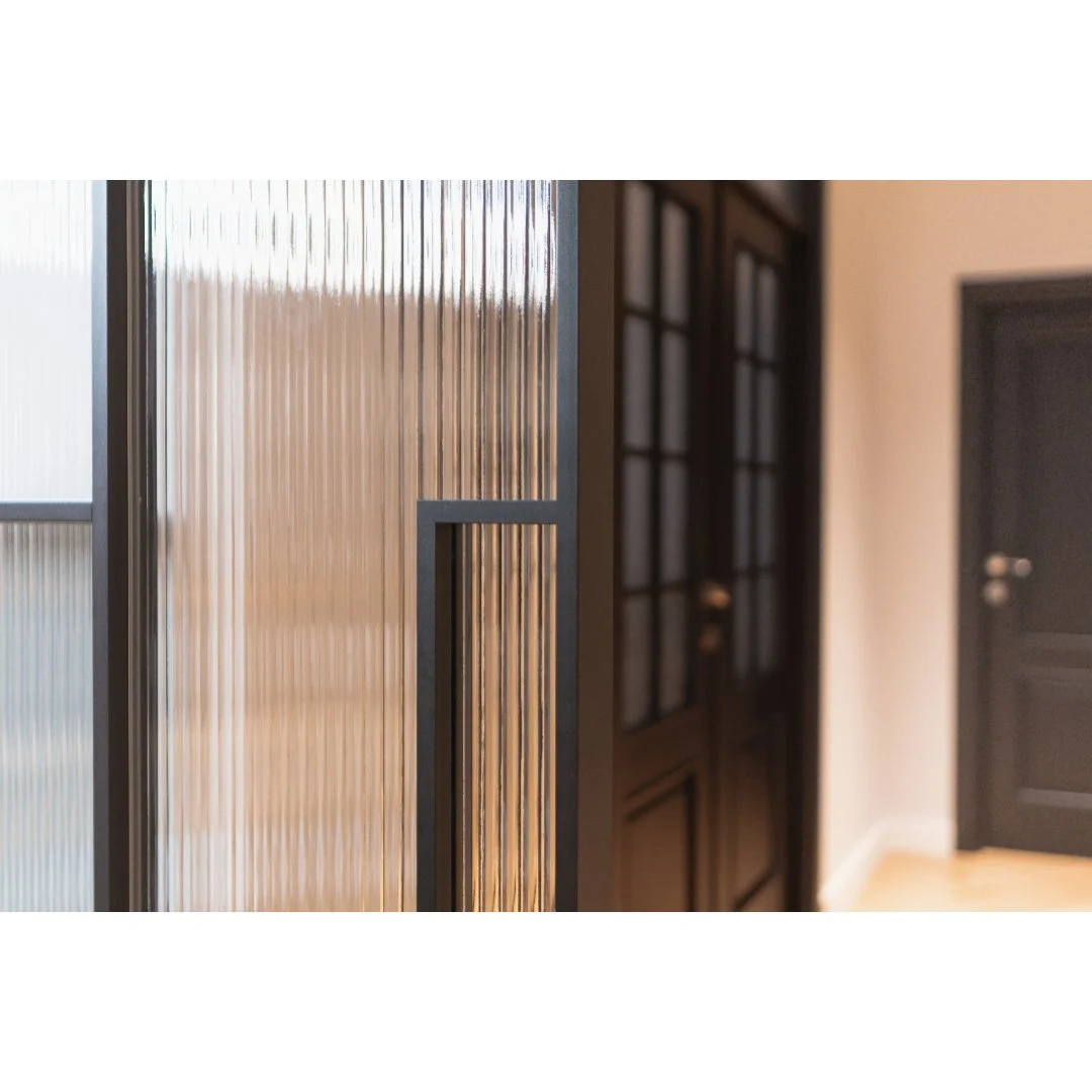 Close-up of a glass door with ribbed glass panels and black metal frame, with a hallway and closed door in the background.
