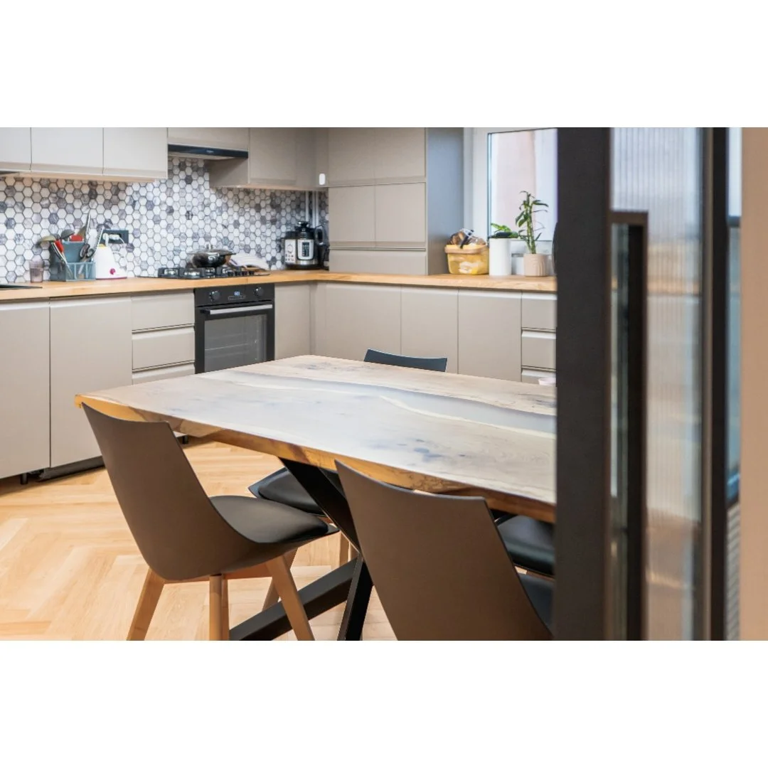 Modern kitchen with light gray cabinets, a wooden countertop, hexagonal tile backsplash, and a dining table with black chairs.