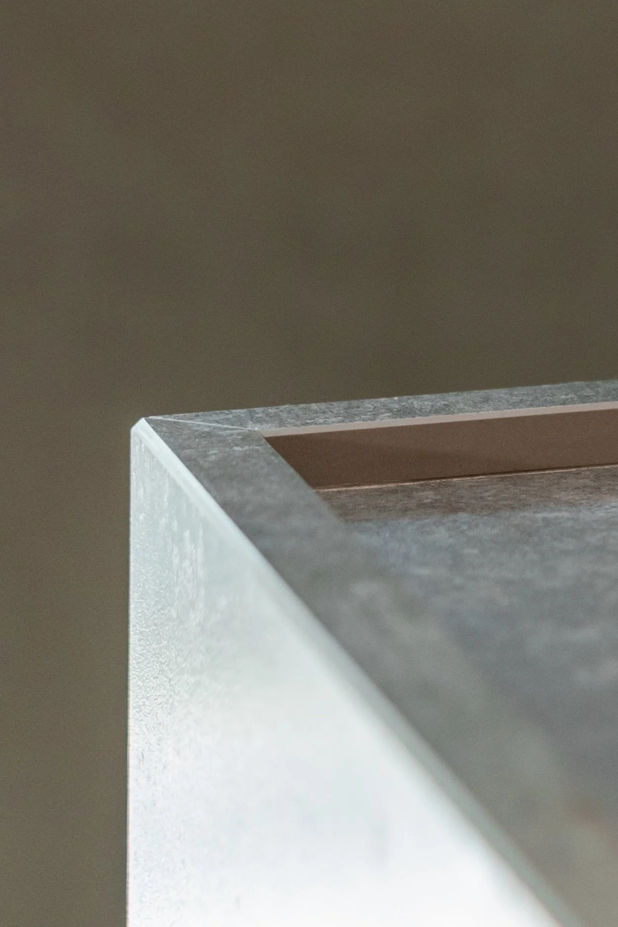 Close-up of a corner of a modern, minimalist table with a textured gray surface and a flat, brown inner border, against a plain background.