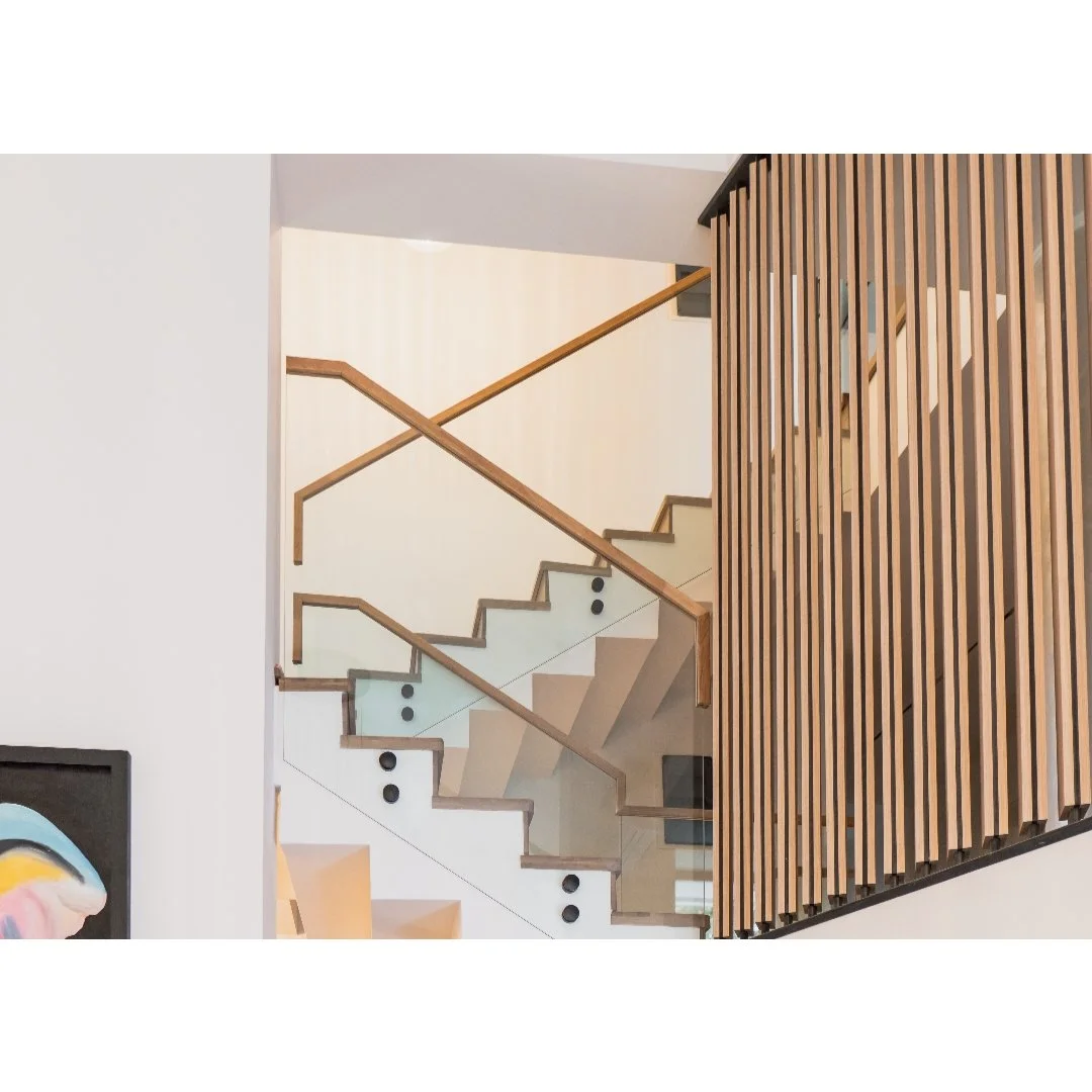 Modern staircase with wooden handrails and glass panels, adjacent to a wooden slatted wall in a contemporary interior space.