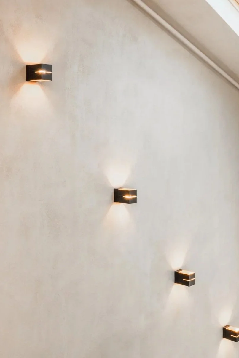 Wall with multiple black square wall sconces that have light emitting upward and downward, creating a pattern of light and shadow.
