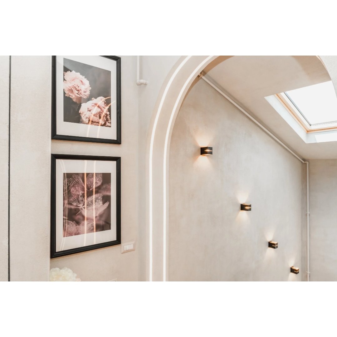 Interior wall with two framed floral photographs, wall sconces, and a ceiling skylight.