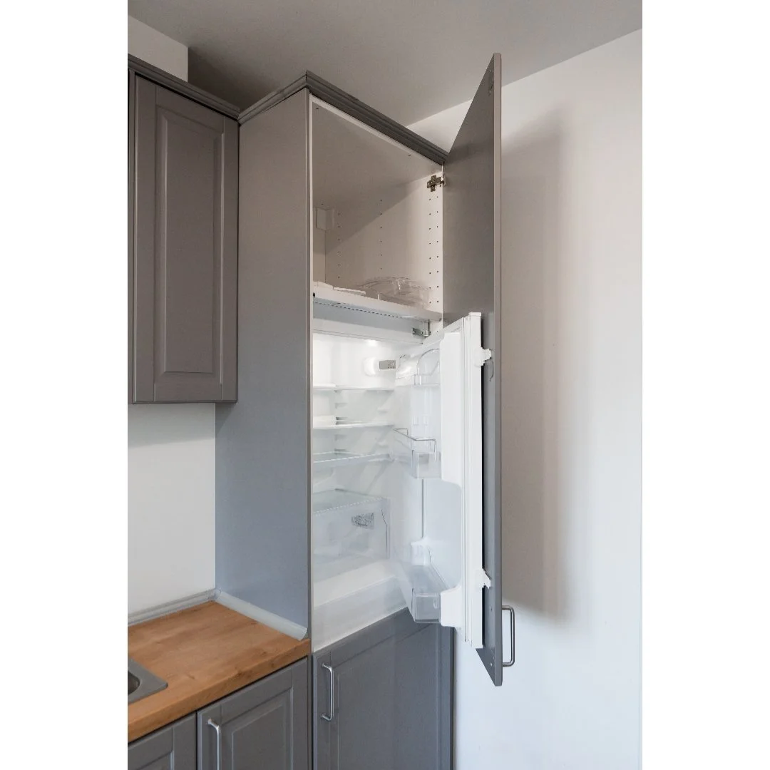 Open refrigerator in a kitchen with gray cabinets and a wooden countertop.