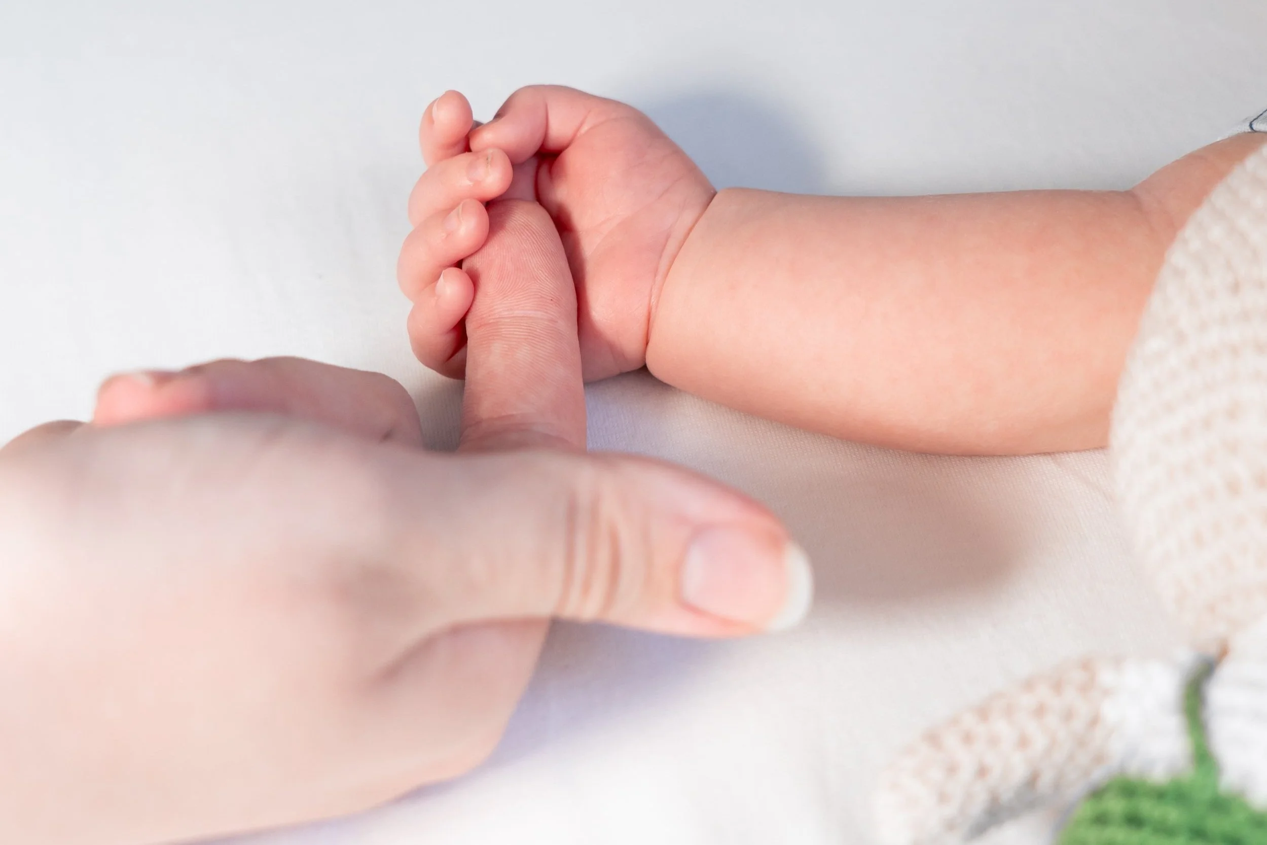 Close-up of an adult's finger touching a baby's finger with both hands resting on a white surface.