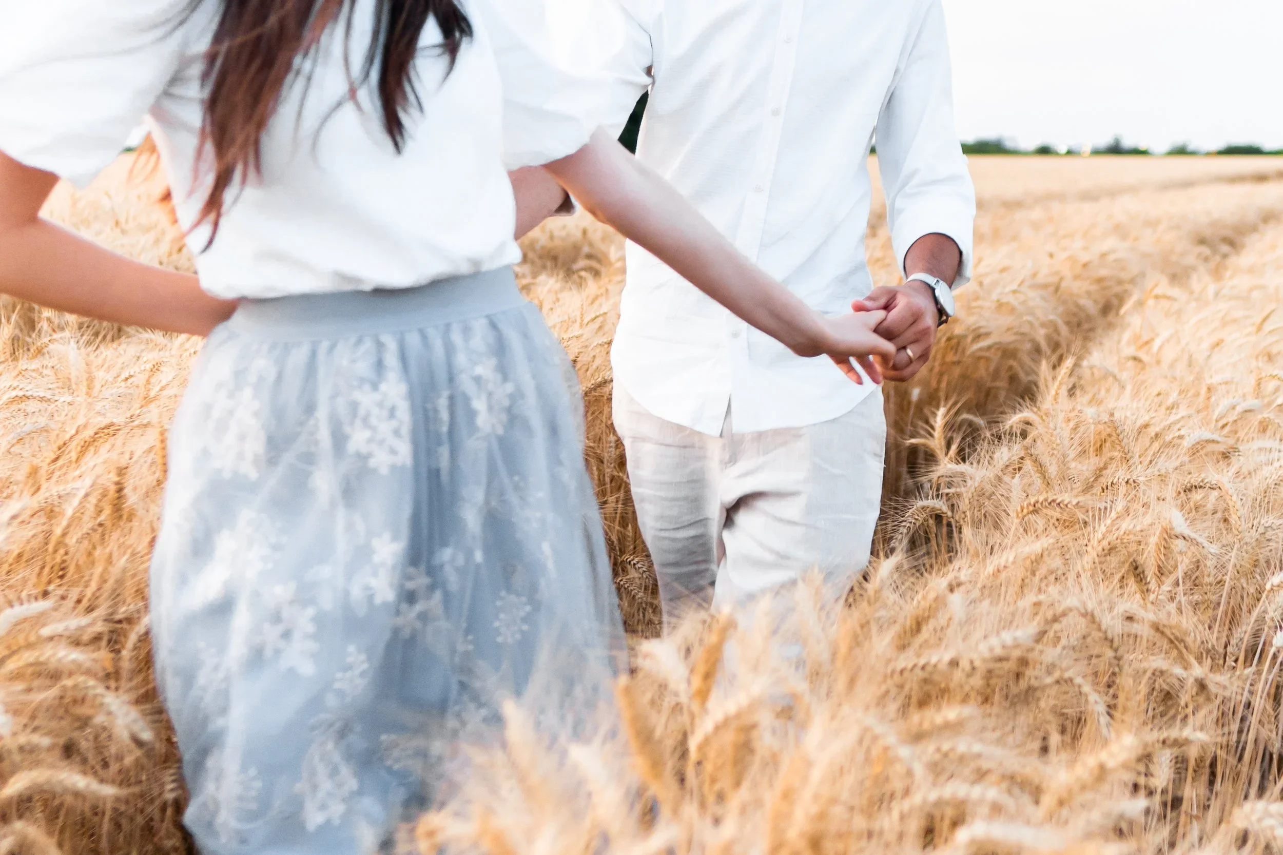 A couple holding hands in a wheat field during daytime