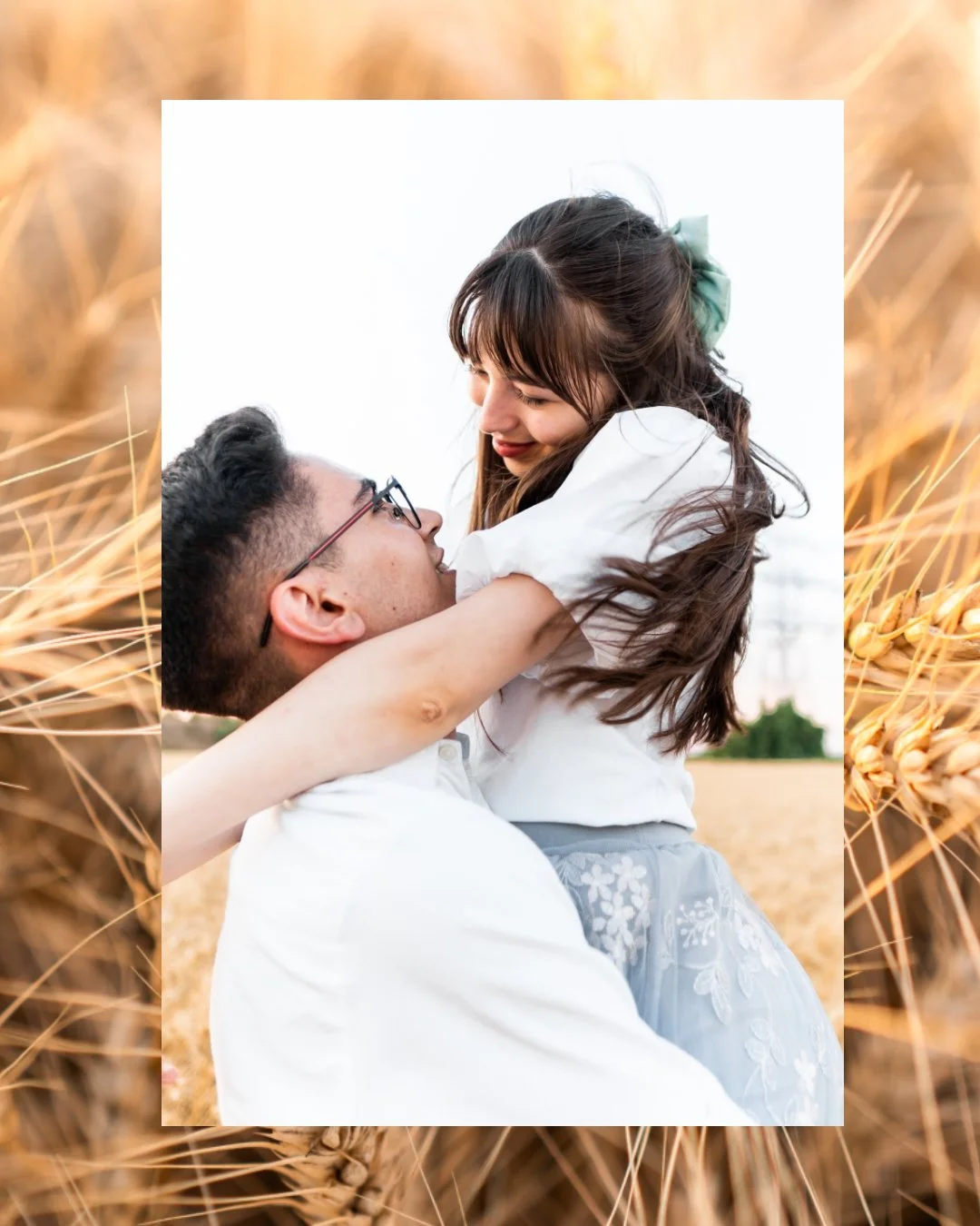 A man lifting a young girl in a wheat field, both smiling and looking at each other.