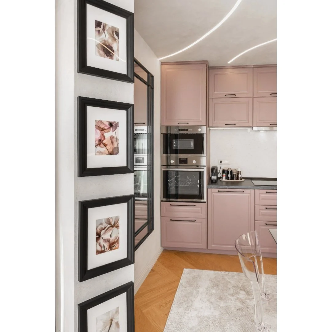 A kitchen with pink cabinets, built-in appliances, and a white countertop. On the left, there are four picture frames with abstract art in black frames.