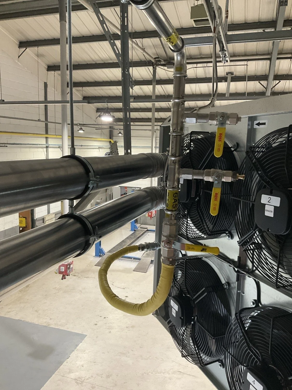Plumbing and heating system with pipes, a red expansion tank, and an electronic control box mounted on a concrete wall.