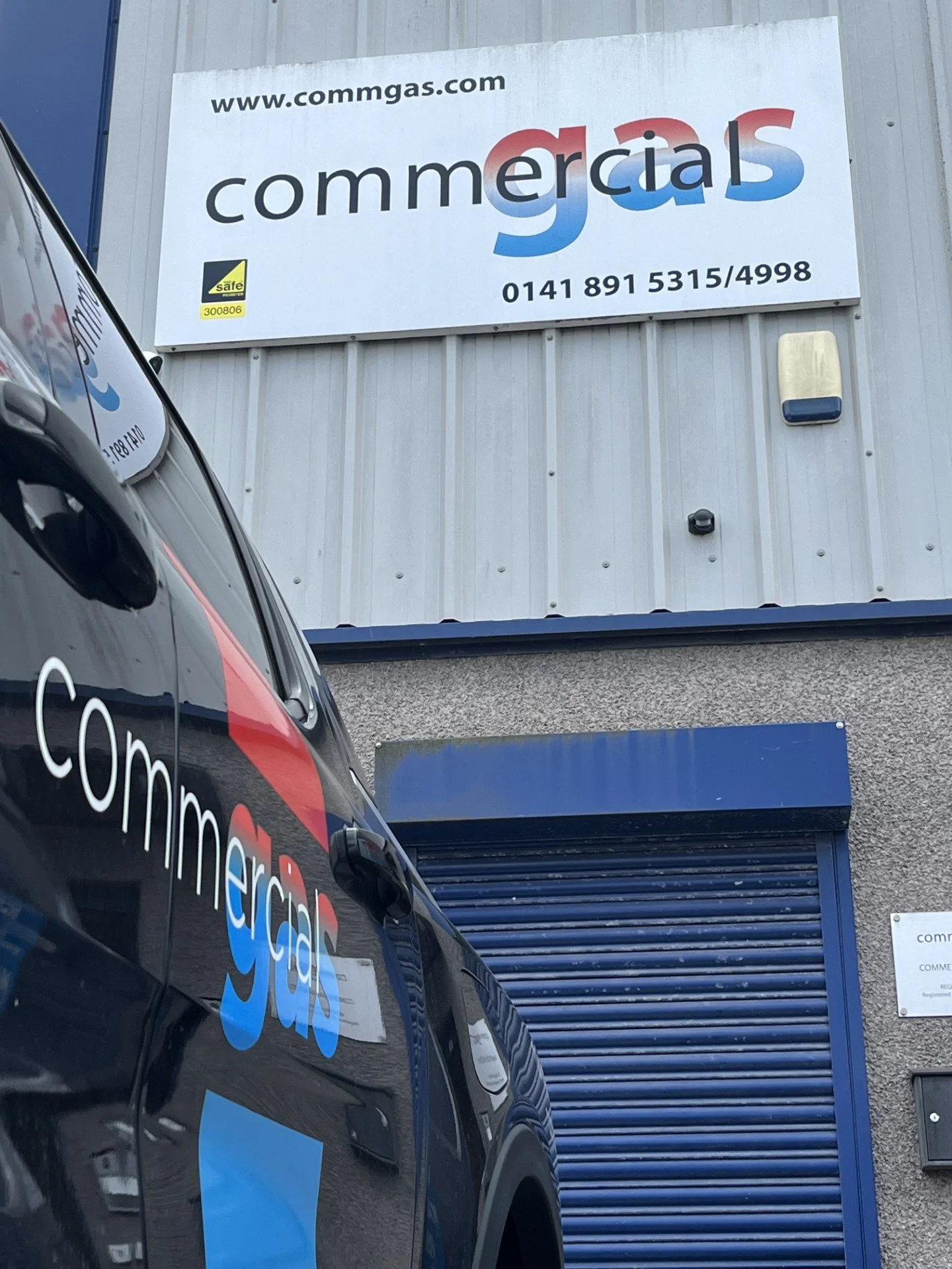 Building exterior with a sign reading "www.commgas.com" and "commercials" with a logo on a vehicle parked outside.