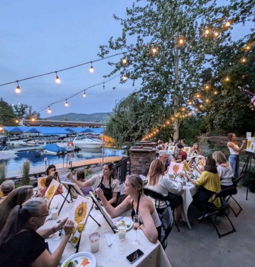 A group of people enjoying a paint and sip night on a beautifully lit outdoor patio.