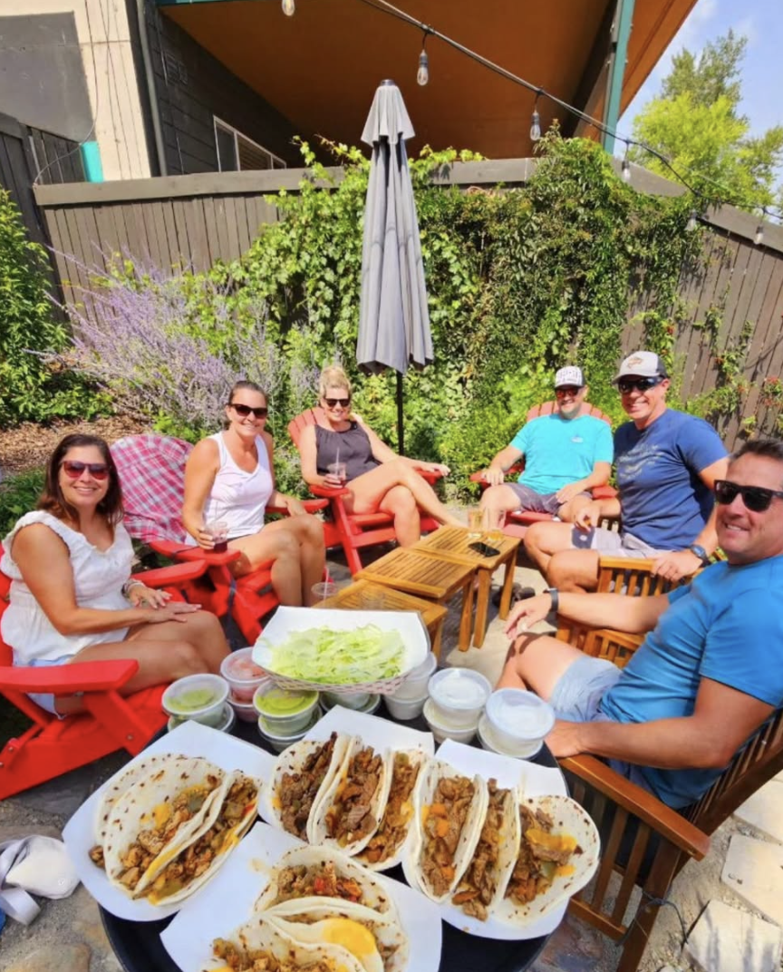 A large group of people on an outside patio with a huge tray of tacos.