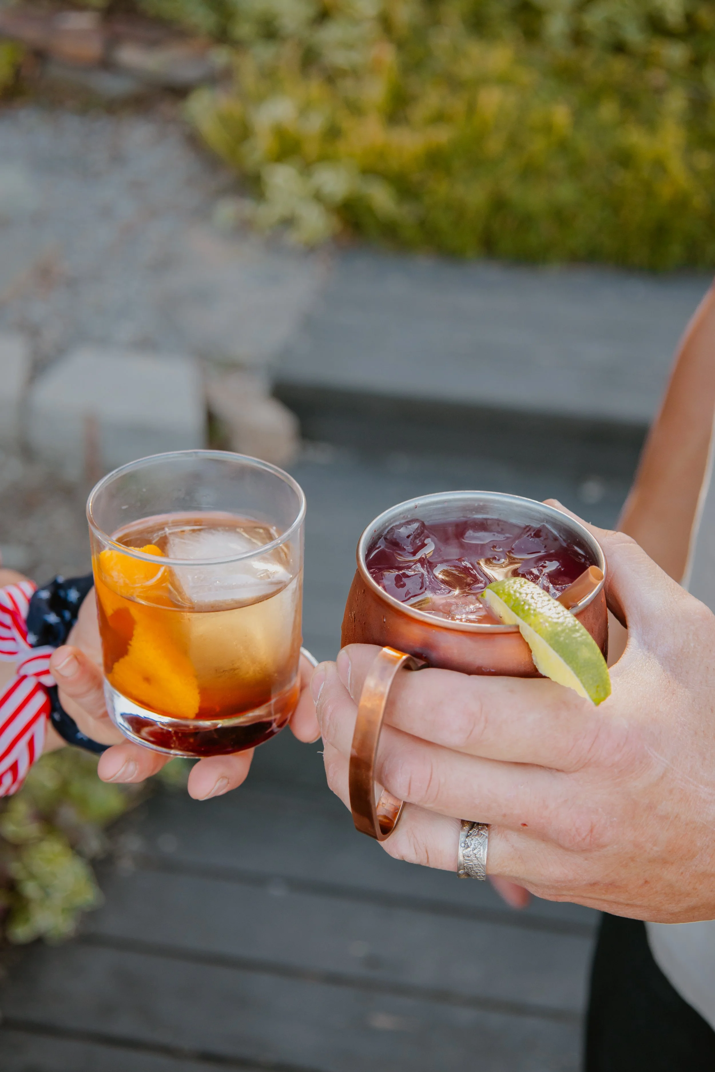 2 people holding 2 elevated cocktails on the patio