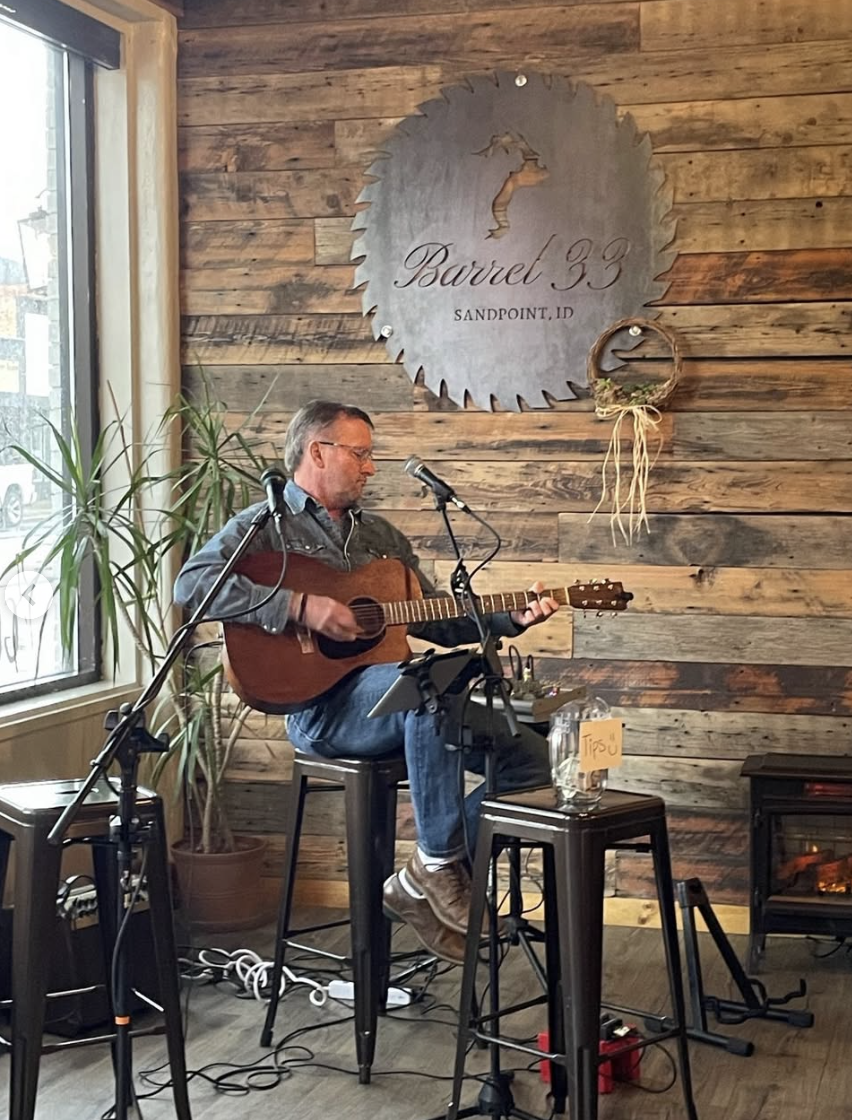 A musician playing guitar under the Barrel 33 sign indoors.