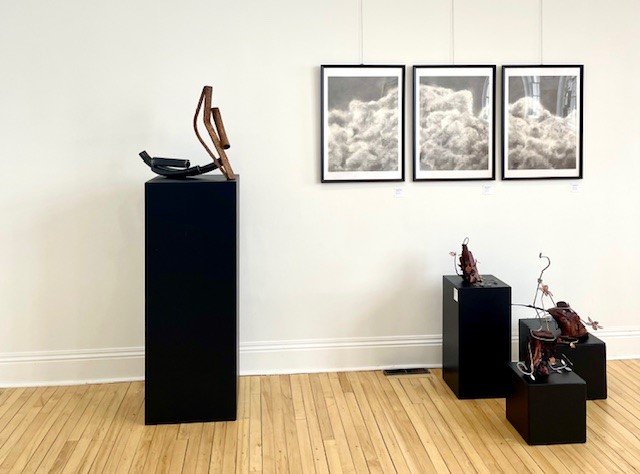 Art gallery displaying sculptures on black pedestals and framed cloud artwork on the wall.