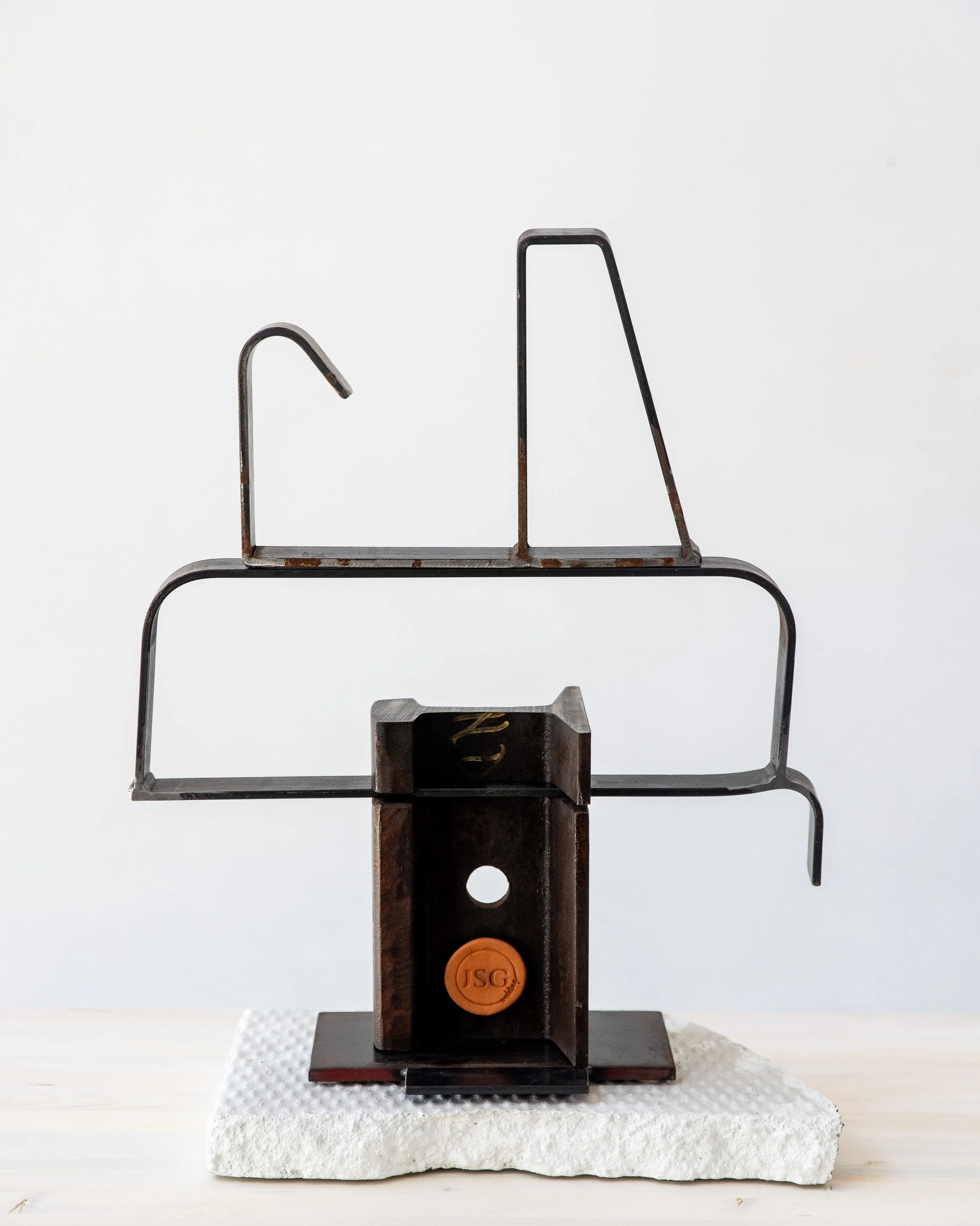 Abstract metal sculpture with geometric shapes on a white surface against a plain light background.