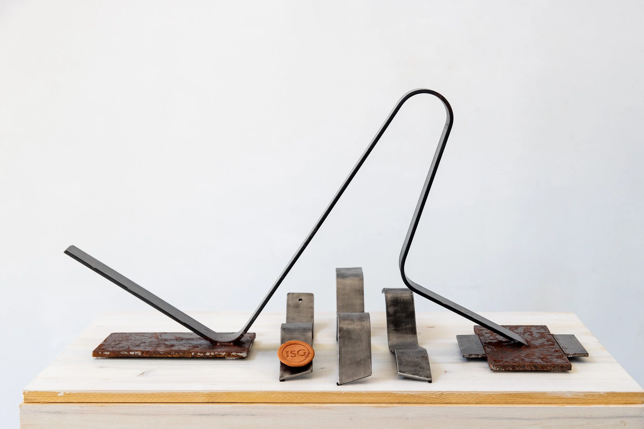 Metal and rusted metal pieces arranged in the shape of a book, mounted on a wooden surface.