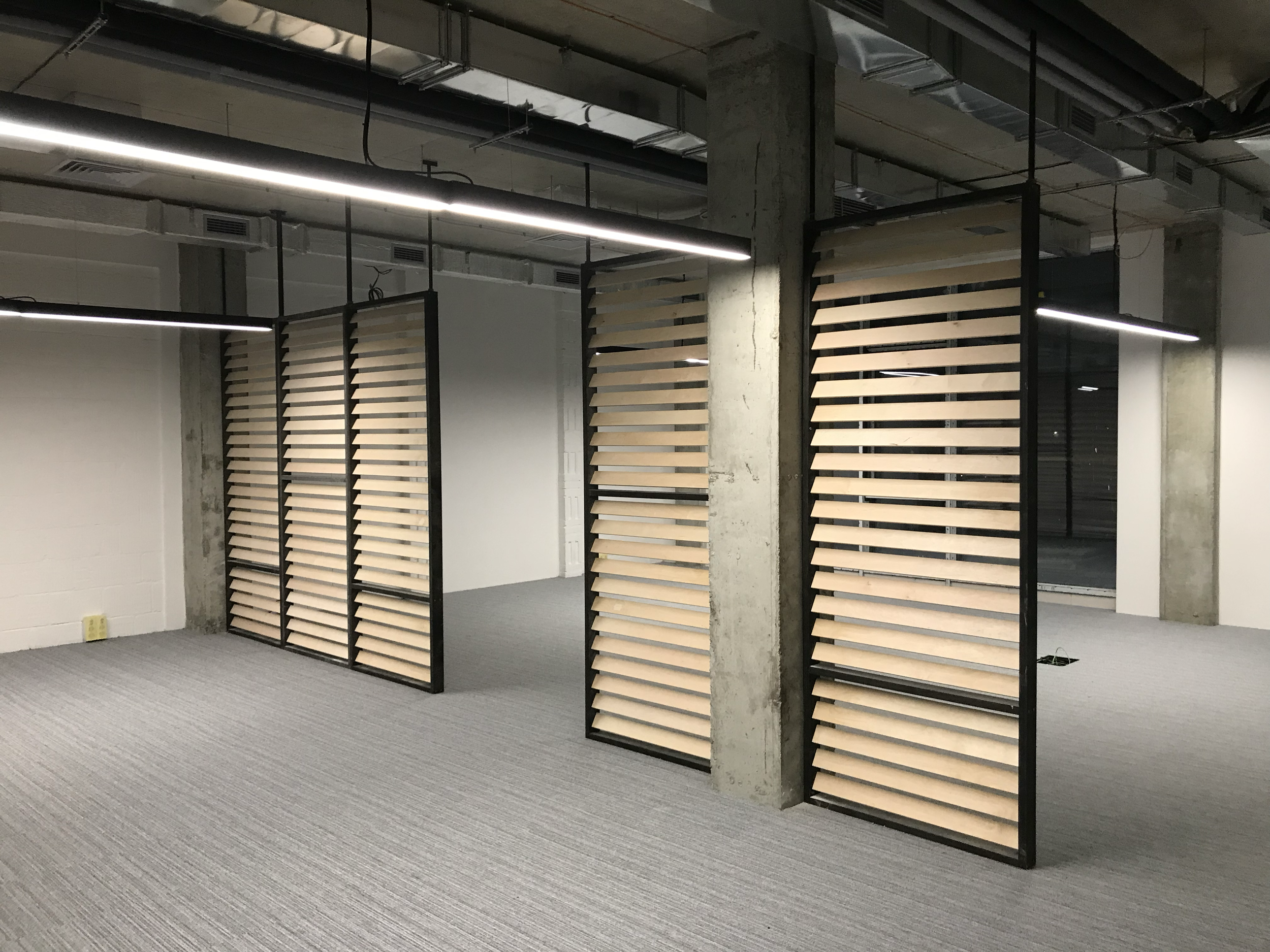 Modern office space with collapsible wooden wall panels, gray carpet, and exposed ceiling with lighting fixtures.