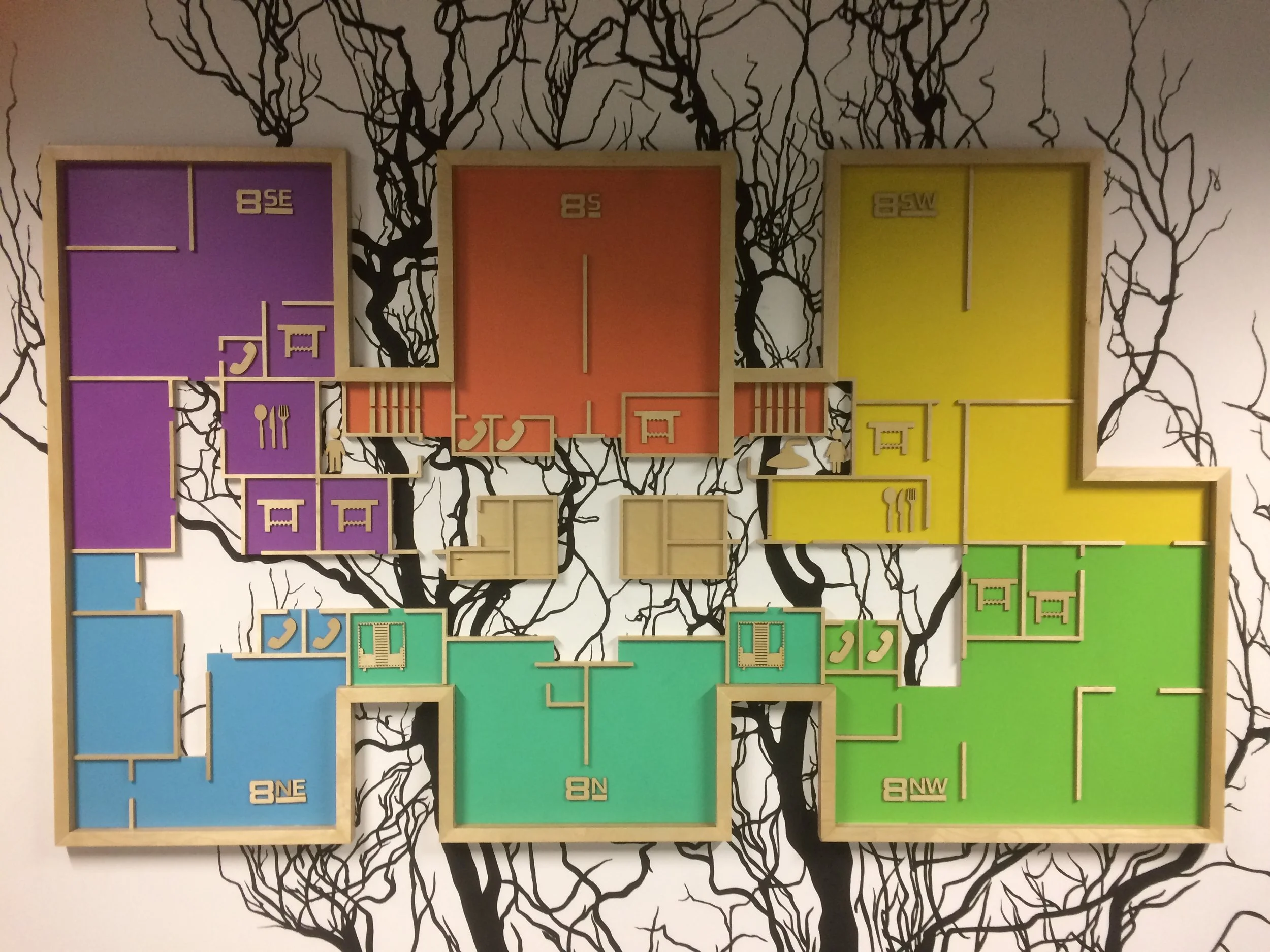 Color-coded wall art design resembling house floor plans arranged in a grid on a black and white tree branch mural wall.
