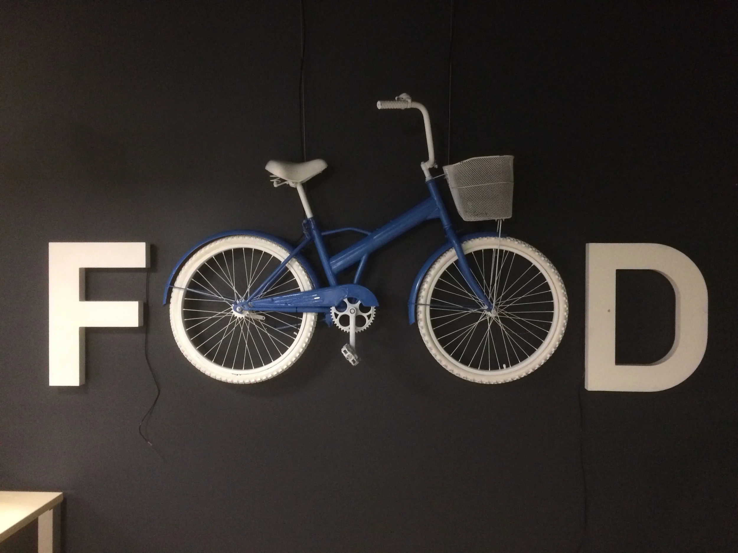 Decorative wall with a blue bicycle mounted between two large white letters, 'F' on the left and 'D' on the right, on a black wall.