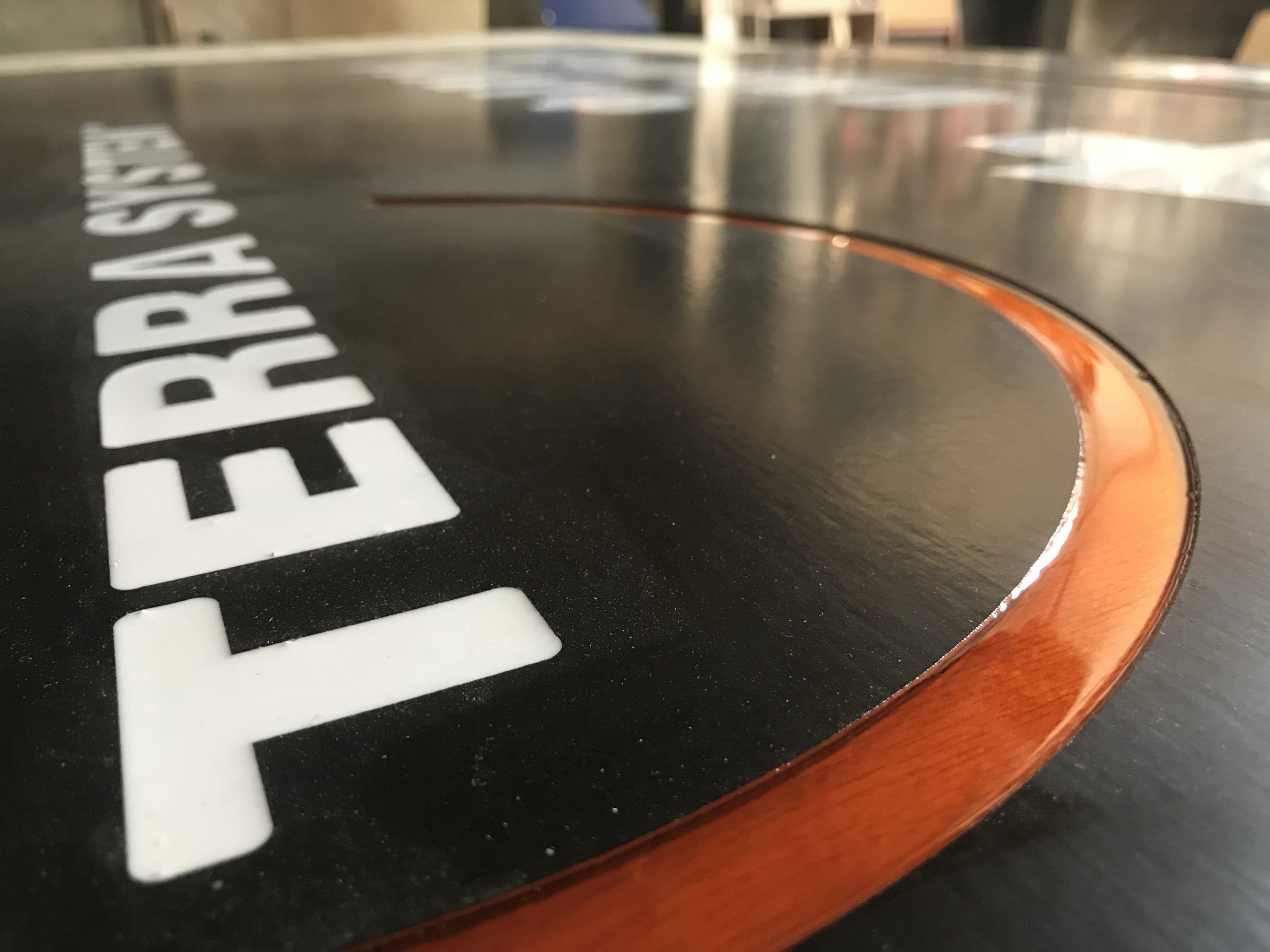 Close-up of a black circular sign with white letters and an orange border, reading 'FERRY BEACH'.