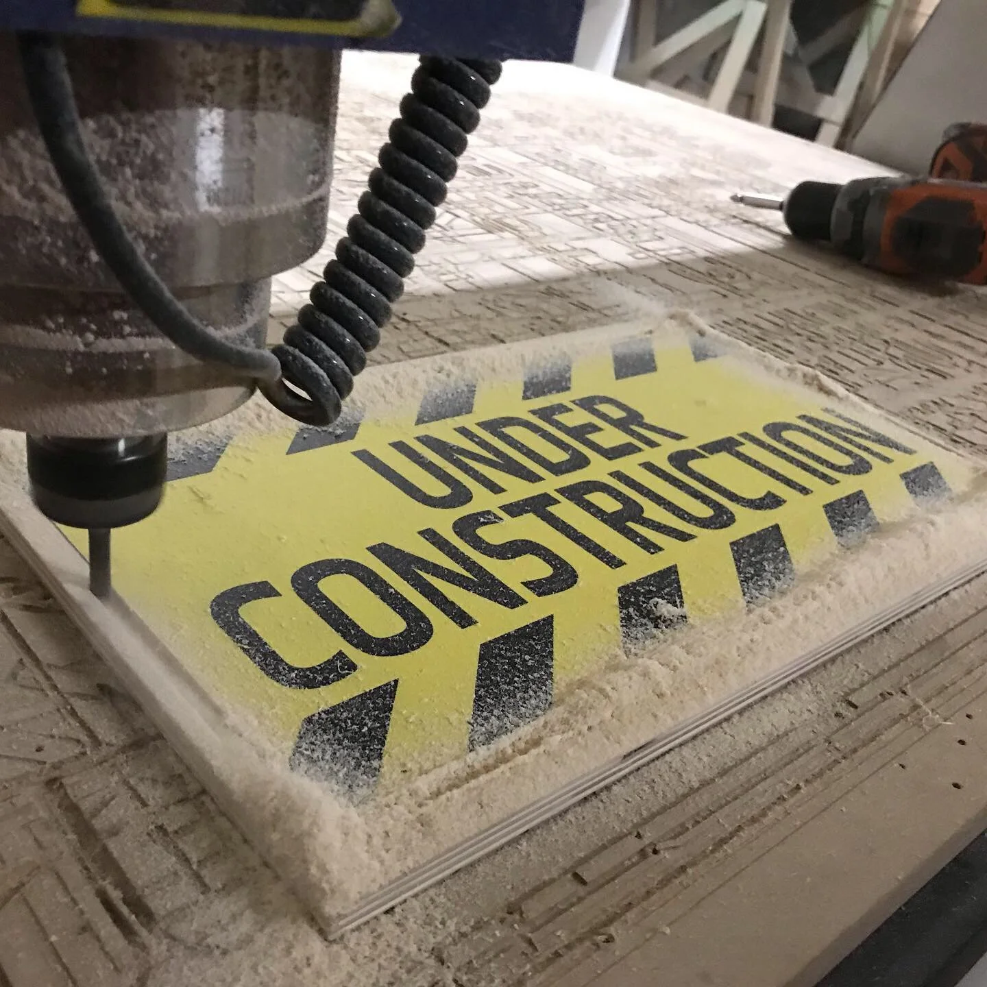 A construction sign with yellow background and black text that reads 'Under Construction' is being engraved or cut into a piece of material, with dust and tools around.