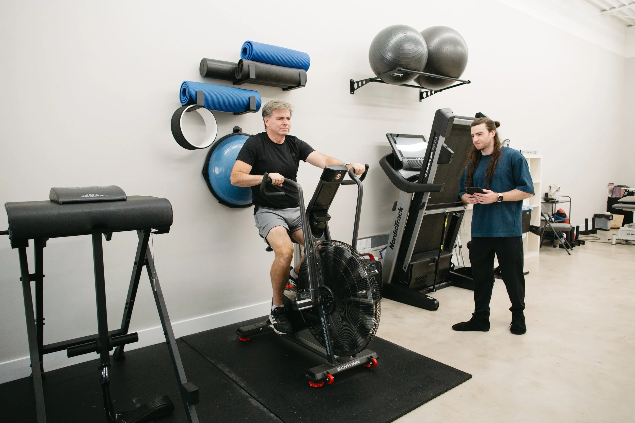 Client performing cardio assessment on assault bike with CoGym coach