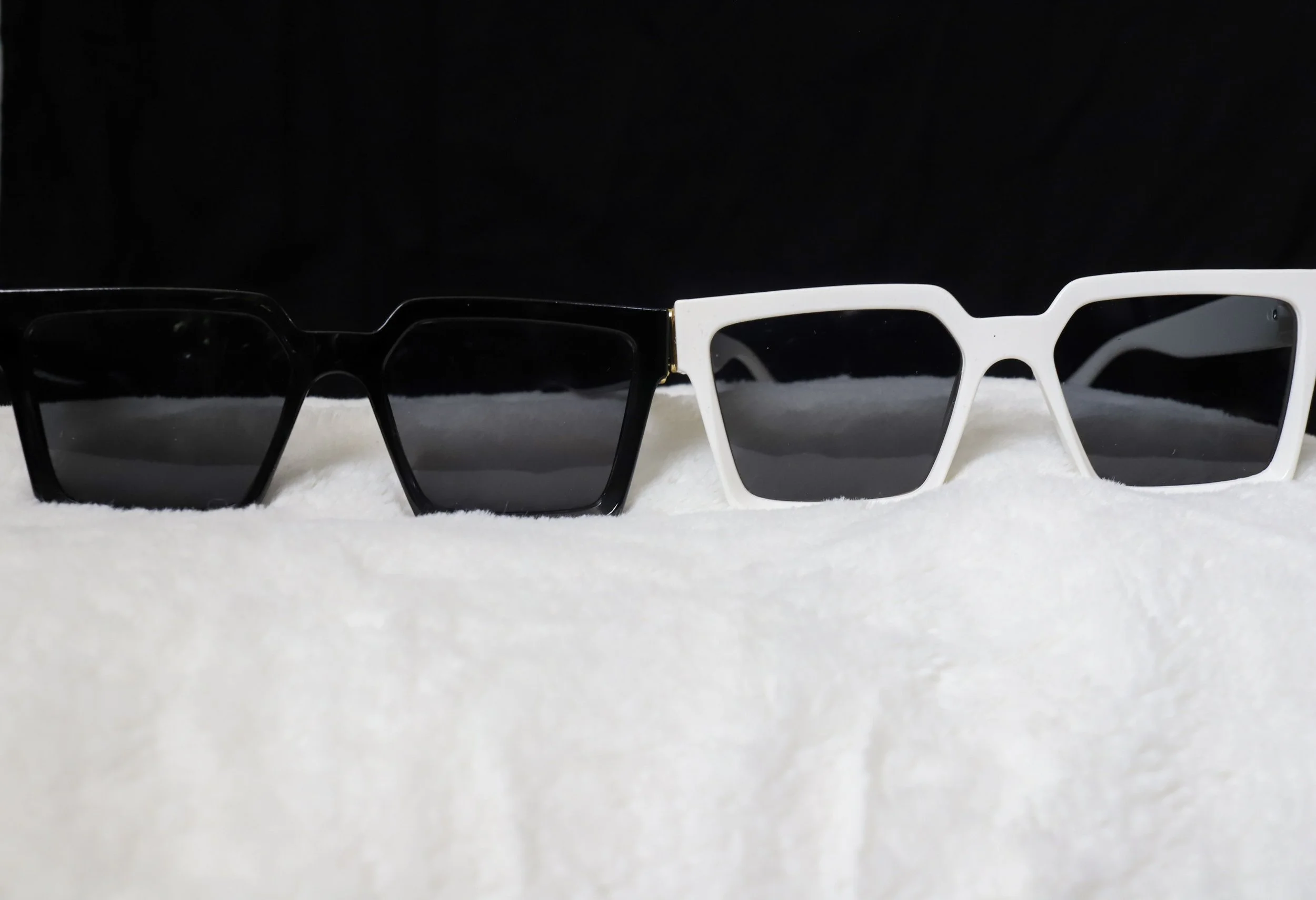 Pair of black sunglasses and white sunglasses with dark lenses on a white surface against a black background.