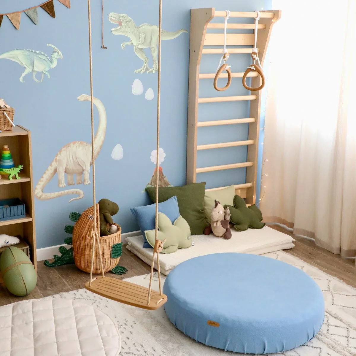 Blau/grünes Kinderzimmer mit weichem Teppich, Spielmatten, Kletterwand, Schaukel und Dino-Wandstickern